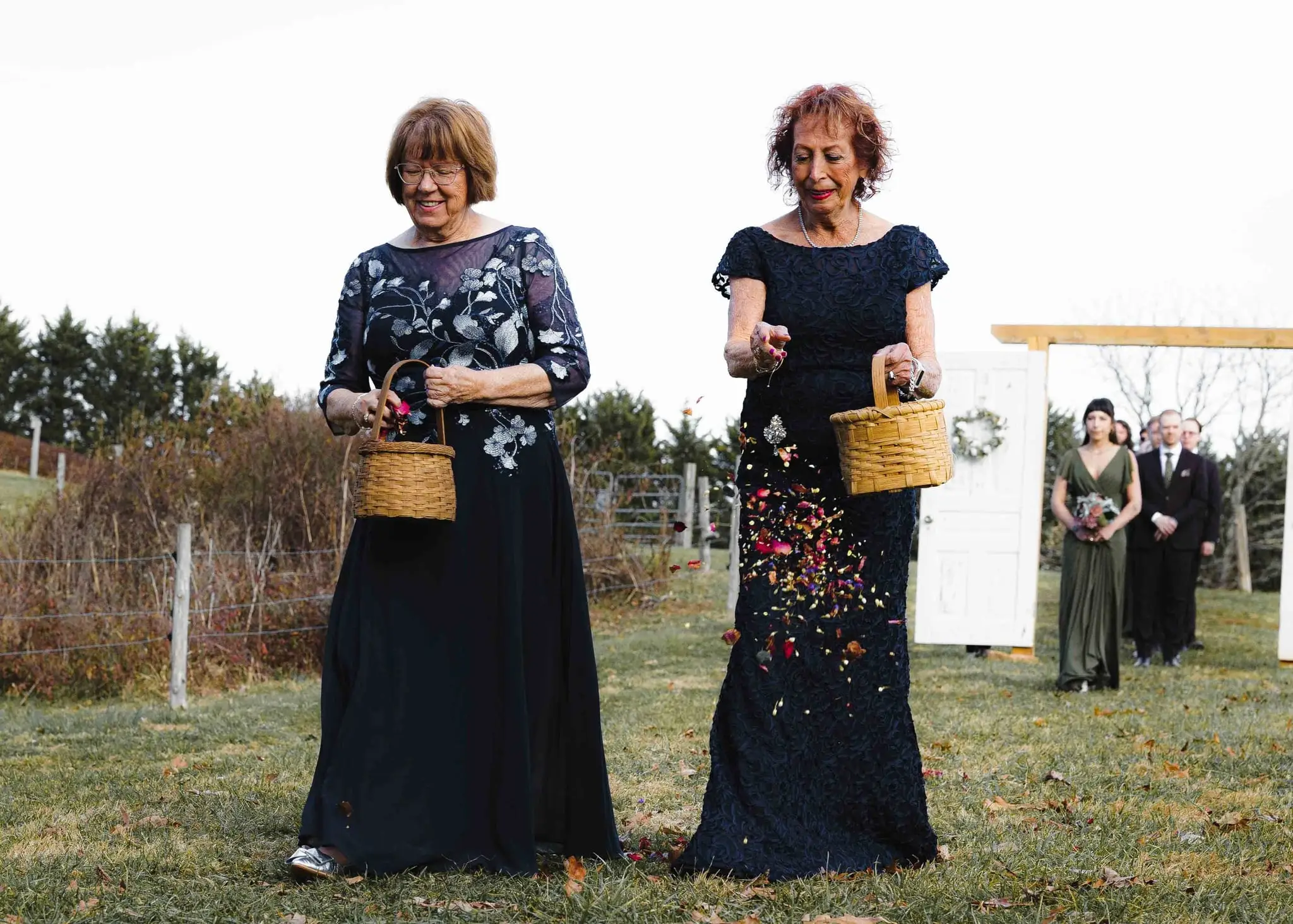 Elizabeth and Aidan wedding at Emerald Ridge Farm, Weaverville NC — two women in navy dresses holding baskets of petals on the lawn