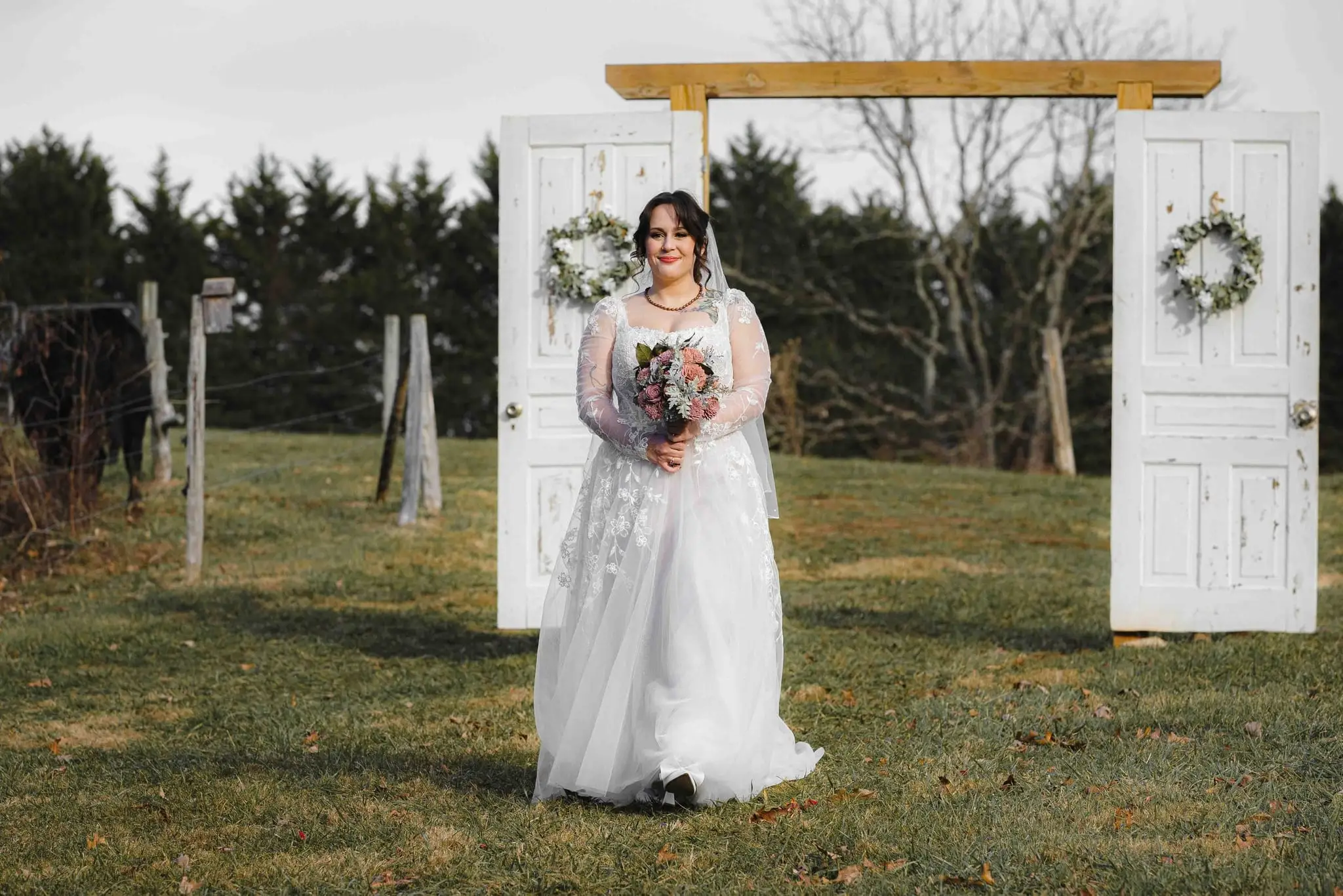 Elizabeth and Aidan wedding at Emerald Ridge Farm, Weaverville NC — the bride walking through the grass past two freestanding white doors