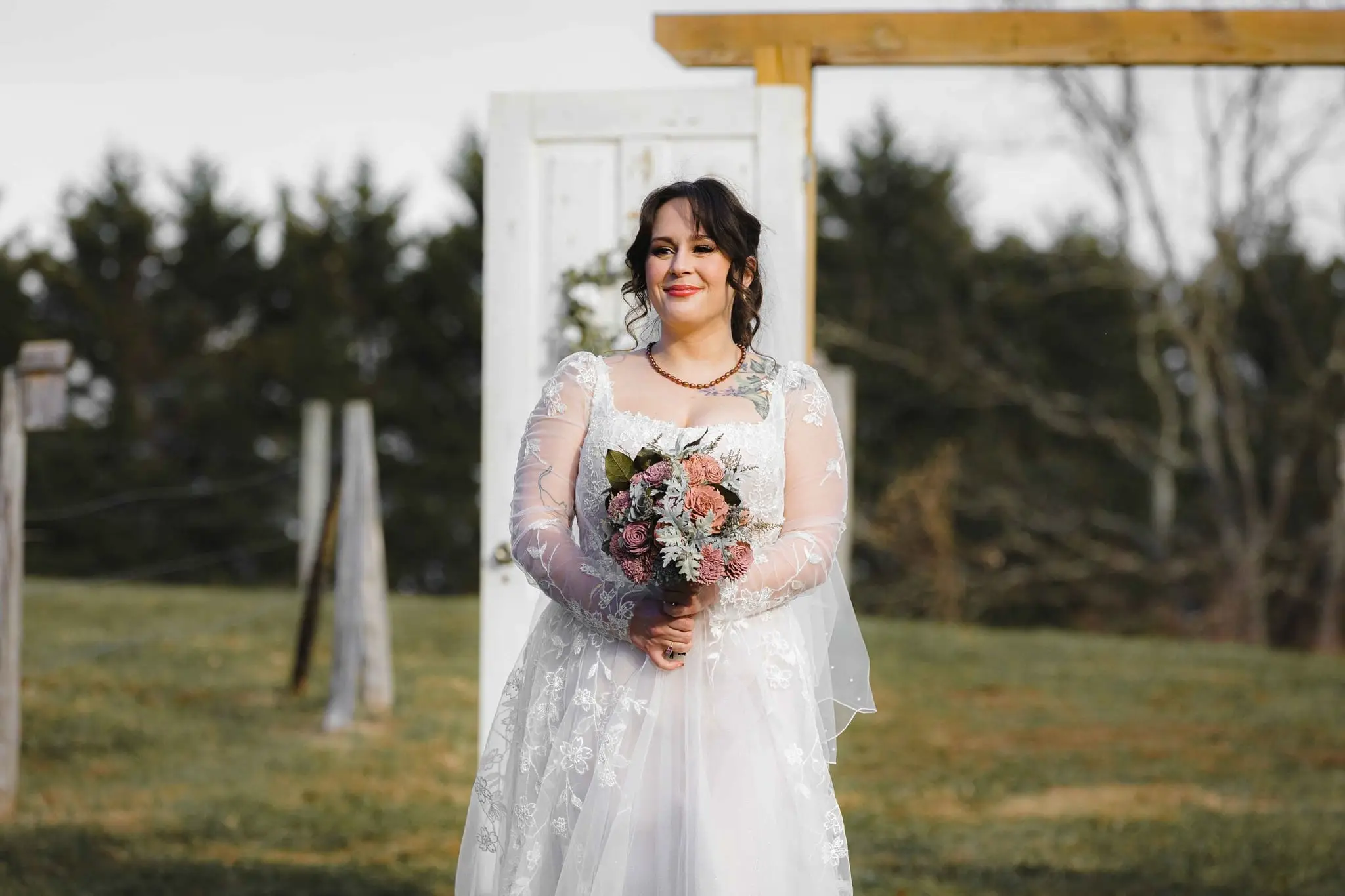 Smiling bride holds a dusty rose bouquet in front of an arch made of white doors