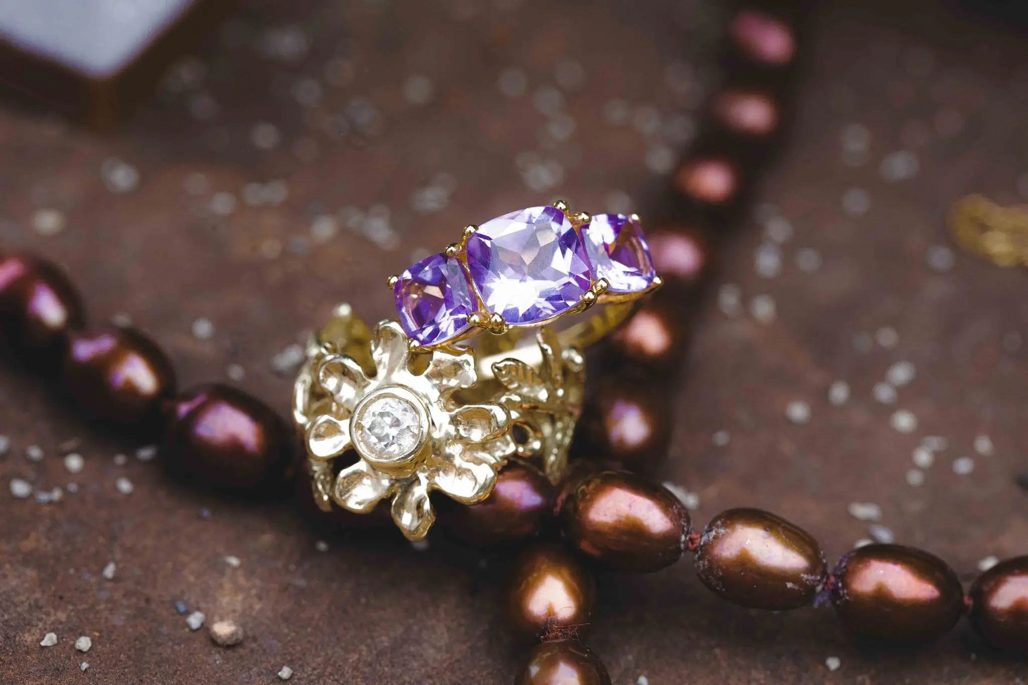 Gold flower-shaped ring with purple amethysts on a strand of deep burgundy pearls