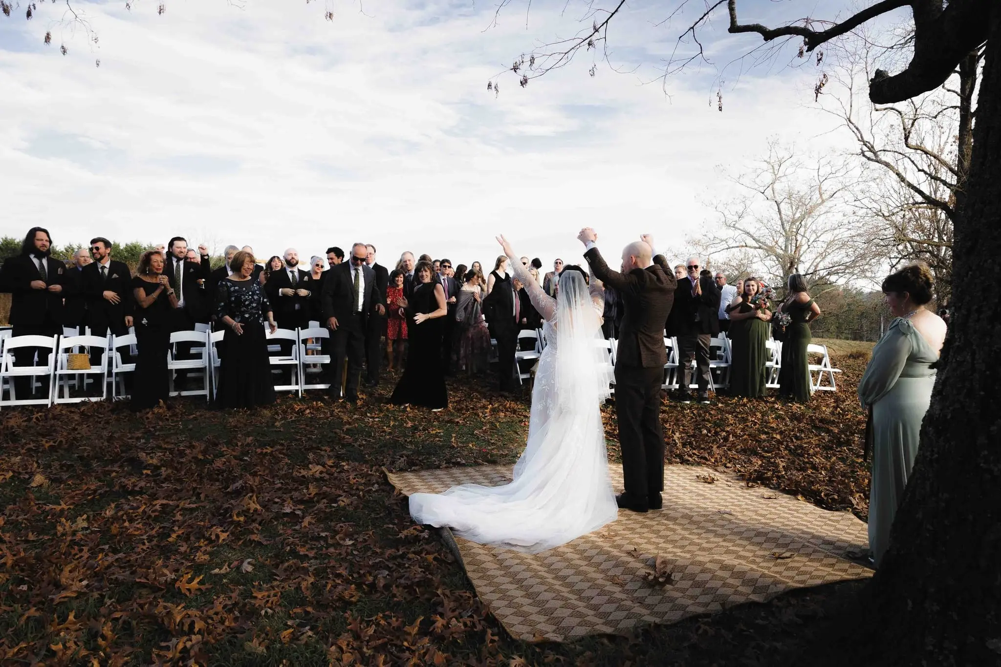 Couple raise their arms in celebration as the whole crowd cheers behind them under the oak