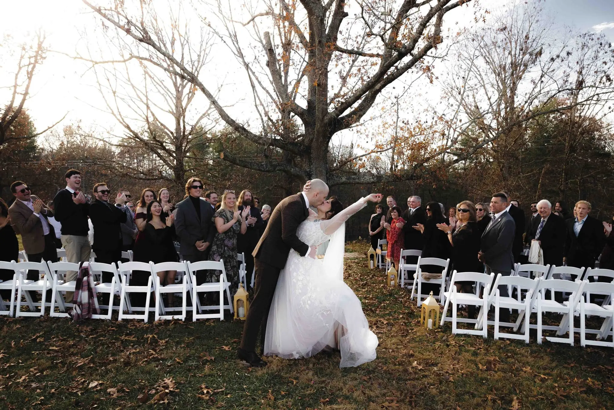 Groom dips the bride for a kiss as guests applaud from white chairs at the outdoor ceremony