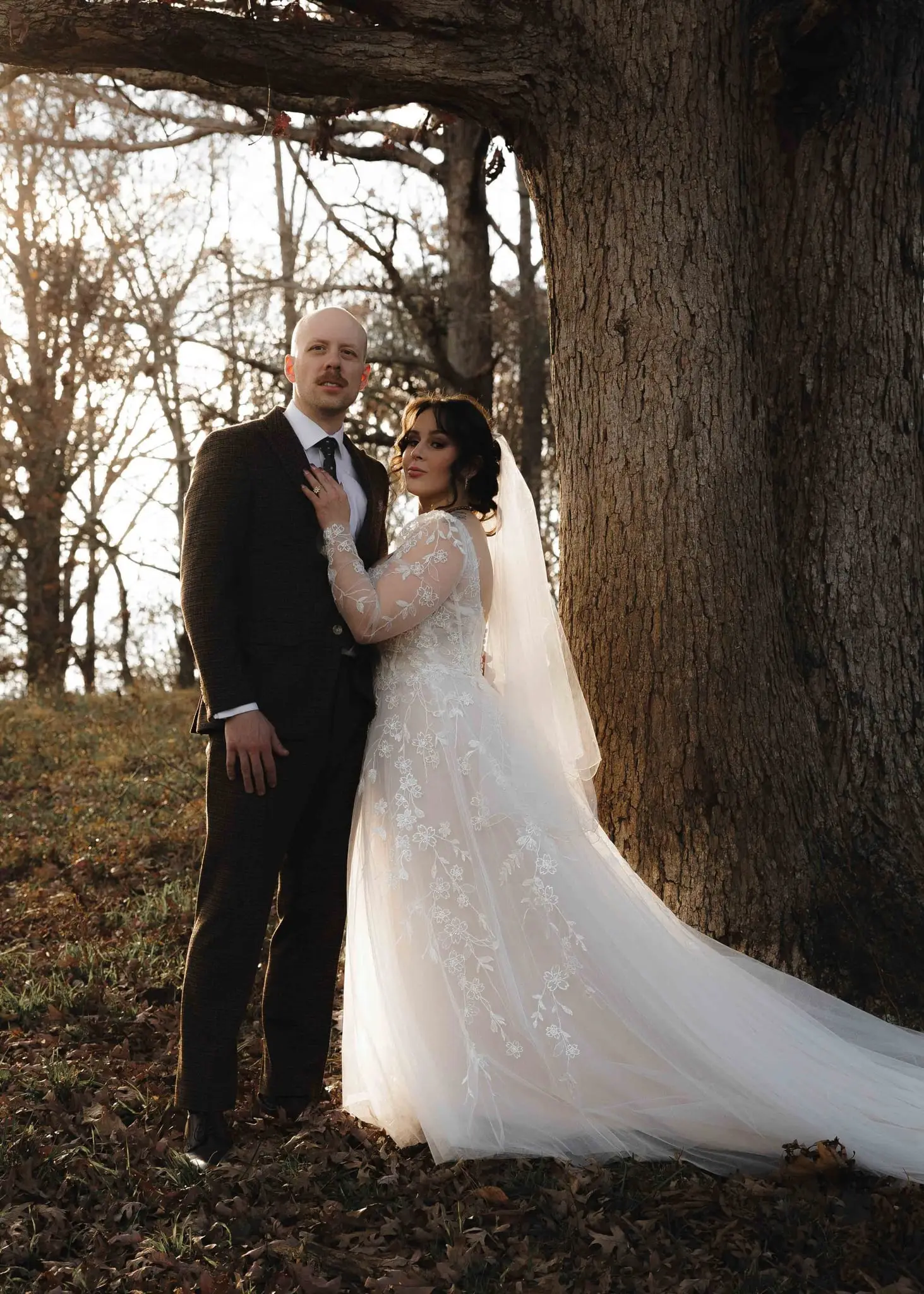 Elizabeth leans on Aidan beside an enormous oak, her lace train trailing on the leaves