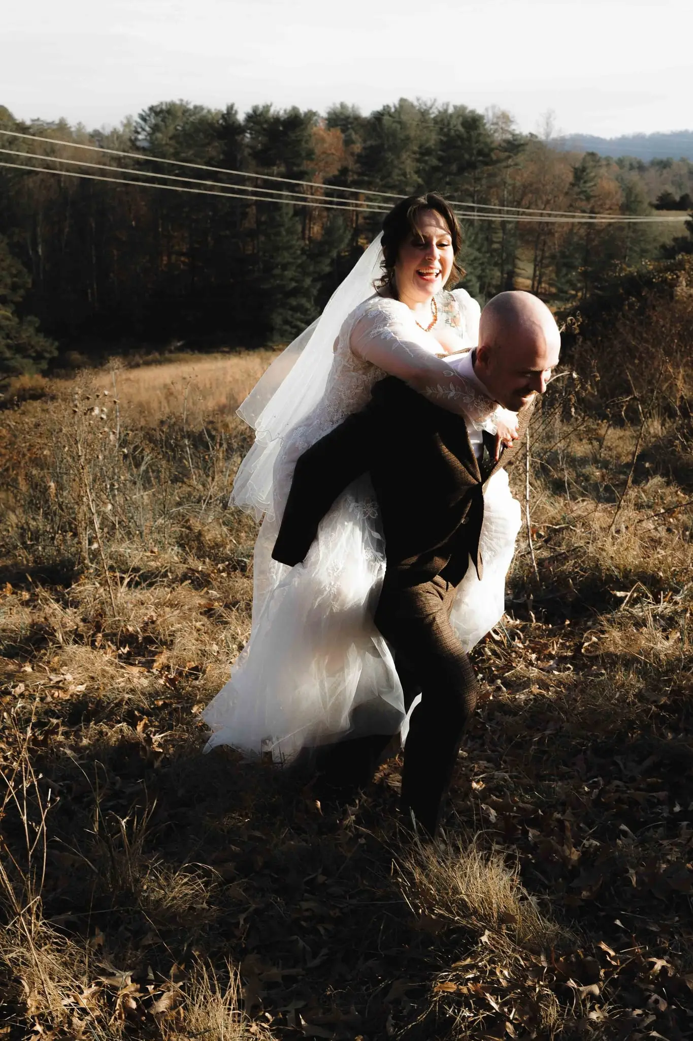 Bride riding piggyback on her groom through a golden field at Emerald Ridge Farm, Weaverville