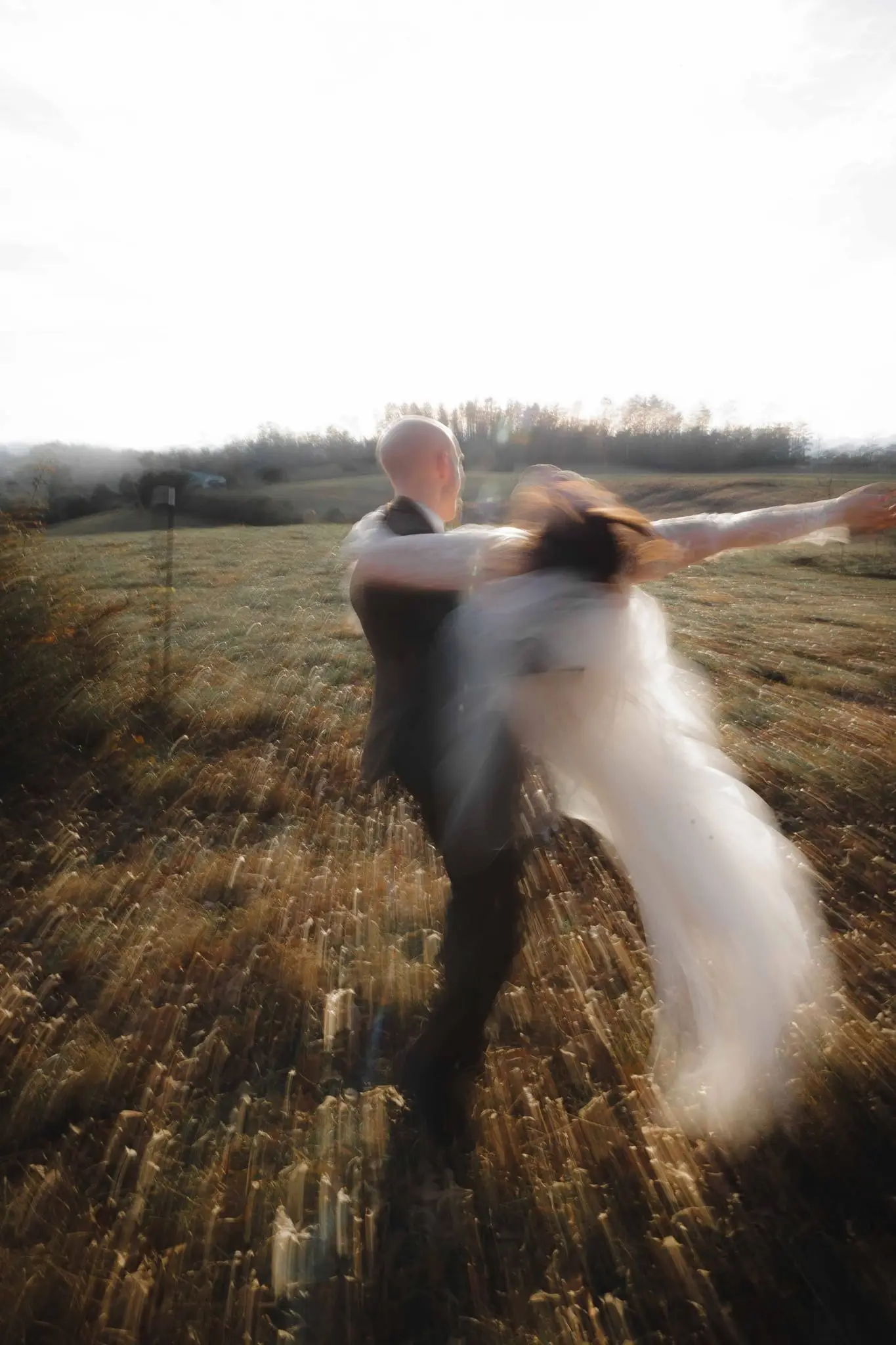 Streaking motion blur of the groom swinging the bride in a field at sunset