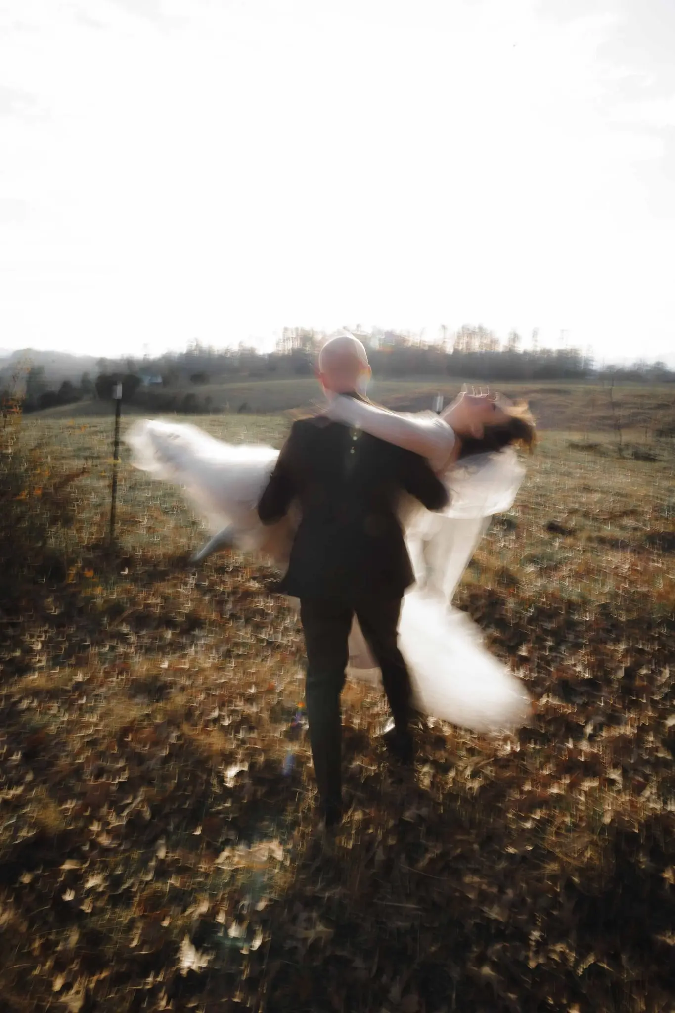 Groom spins the bride in a blur of tulle across a leaf-covered pasture