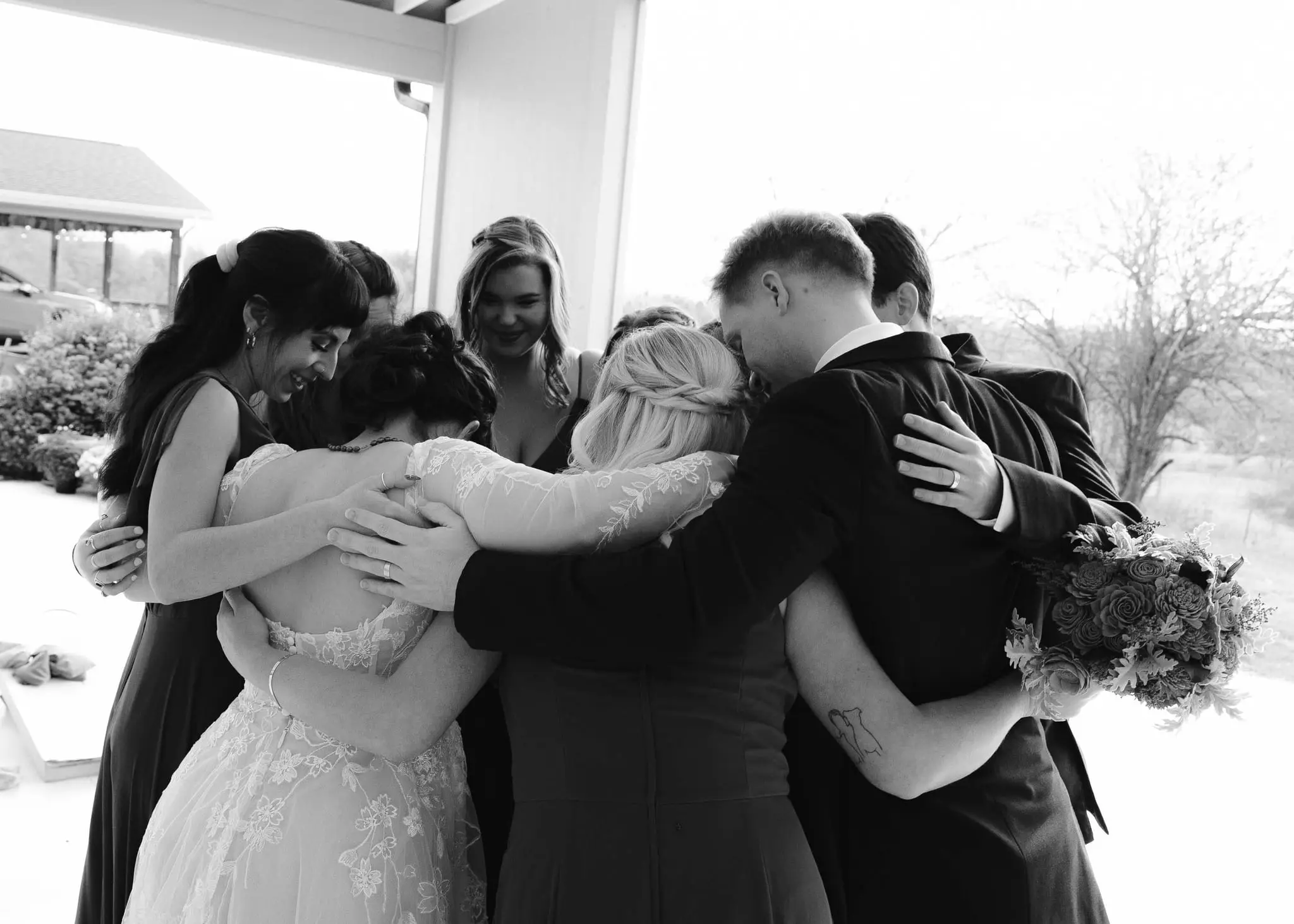 Black and white group hug between the bride, groom and bridesmaids on a porch before the ceremony