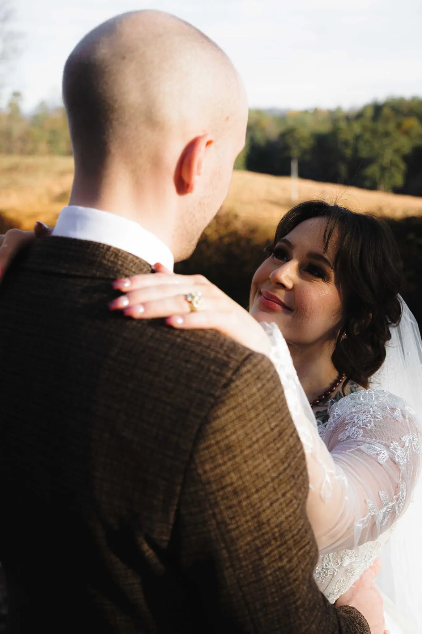 Bride smiles up at the groom with her ring hand on his shoulder in the afternoon sun