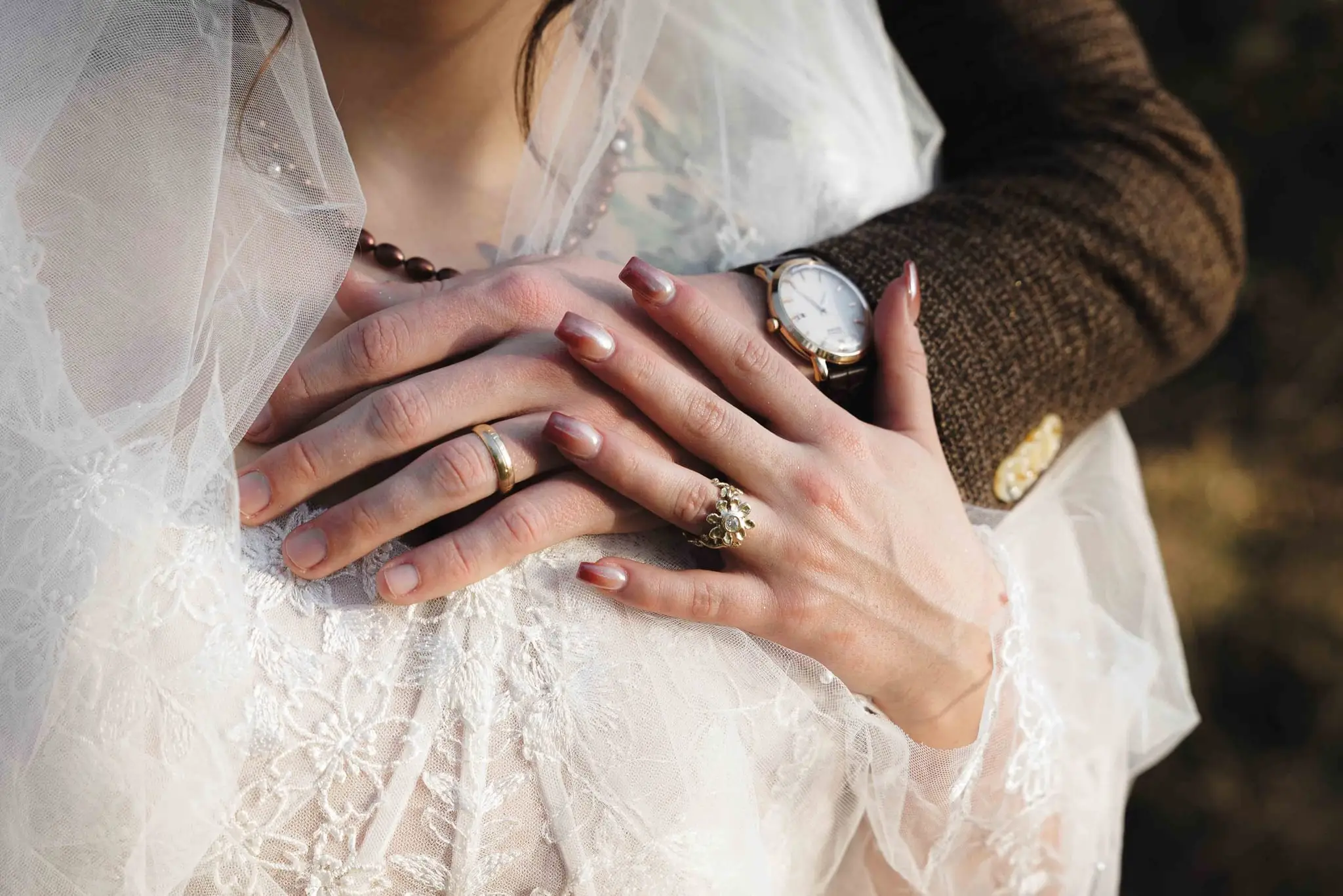 Close-up of a couple’s hands with wedding rings resting on a lace gown
