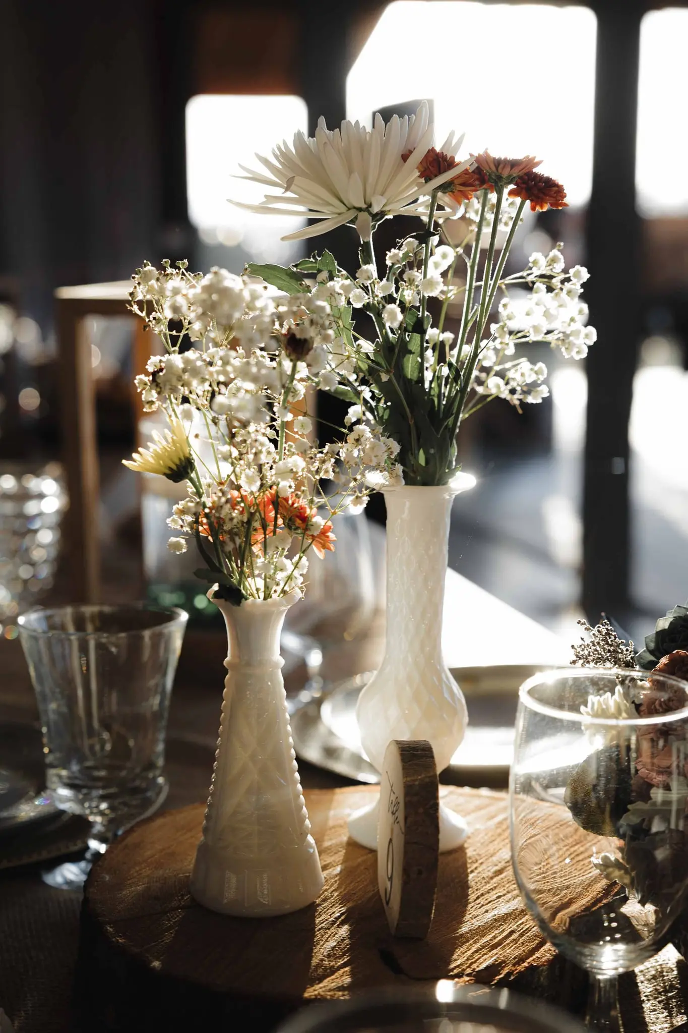 Wildflowers in white milk glass vases on a rustic reception table
