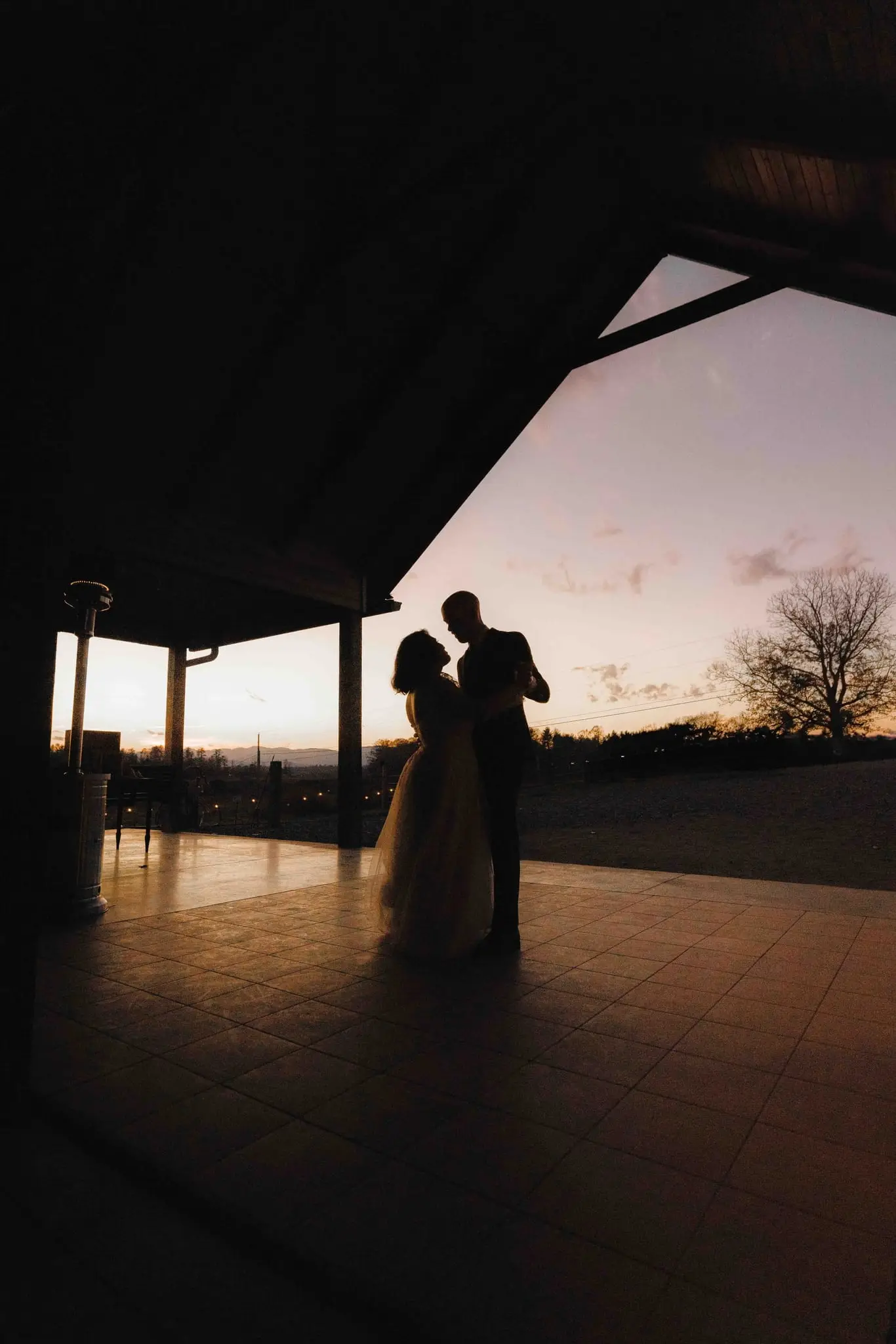 Silhouette of the couple dancing on a covered patio against a pink sunset sky