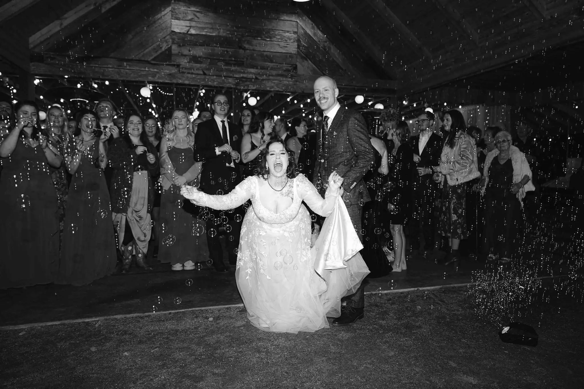 Black and white shot of the bride cheering with her dress lifted as guests toss glitter