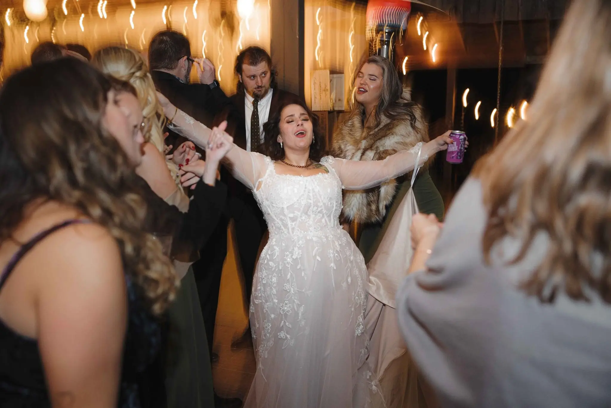Bride sings with her arms spread wide among dancing guests at the reception
