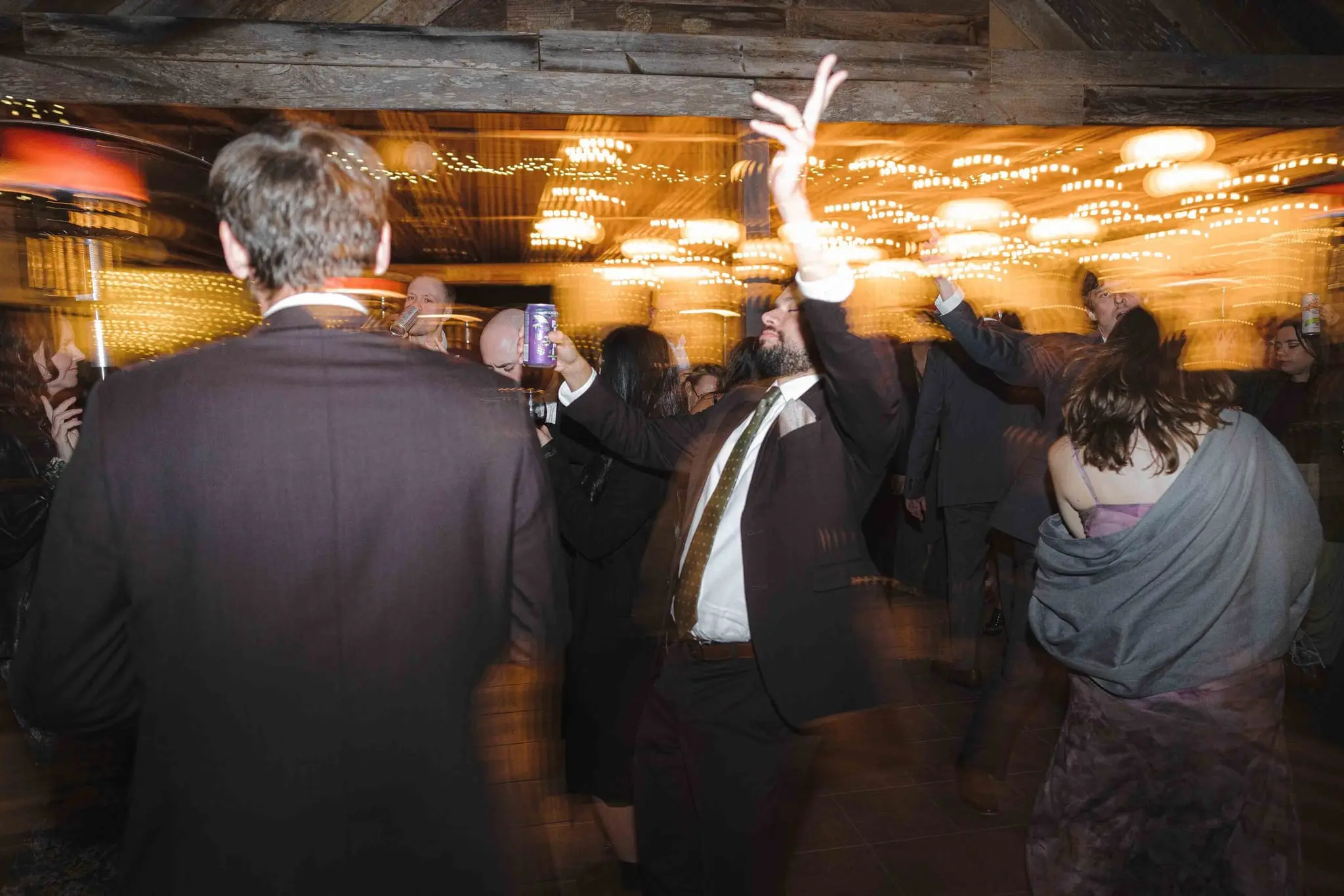 Guest throws an arm in the air on a crowded dance floor beneath strings of lights