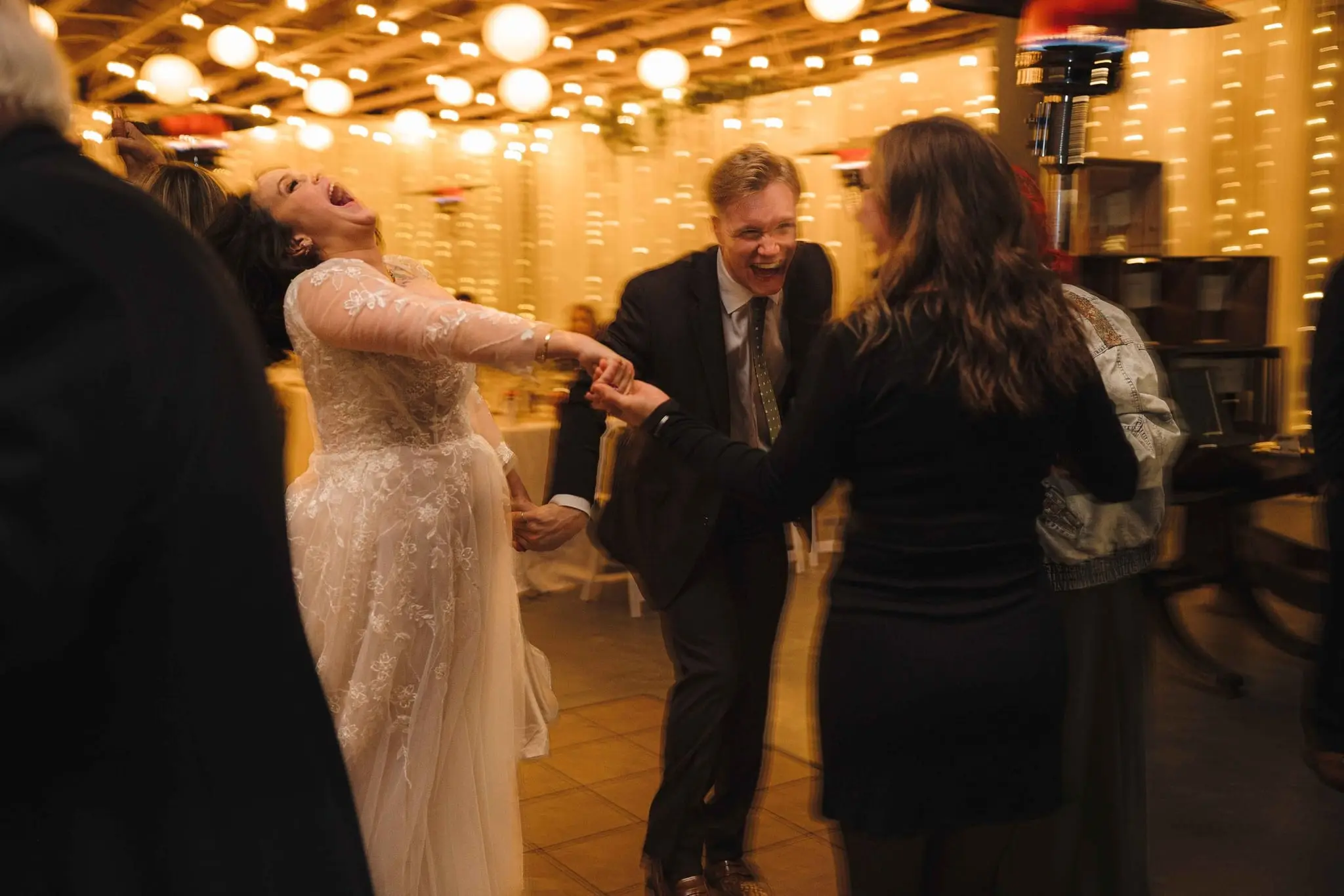 Bride laughs with her head thrown back as she dances hand in hand with a guest