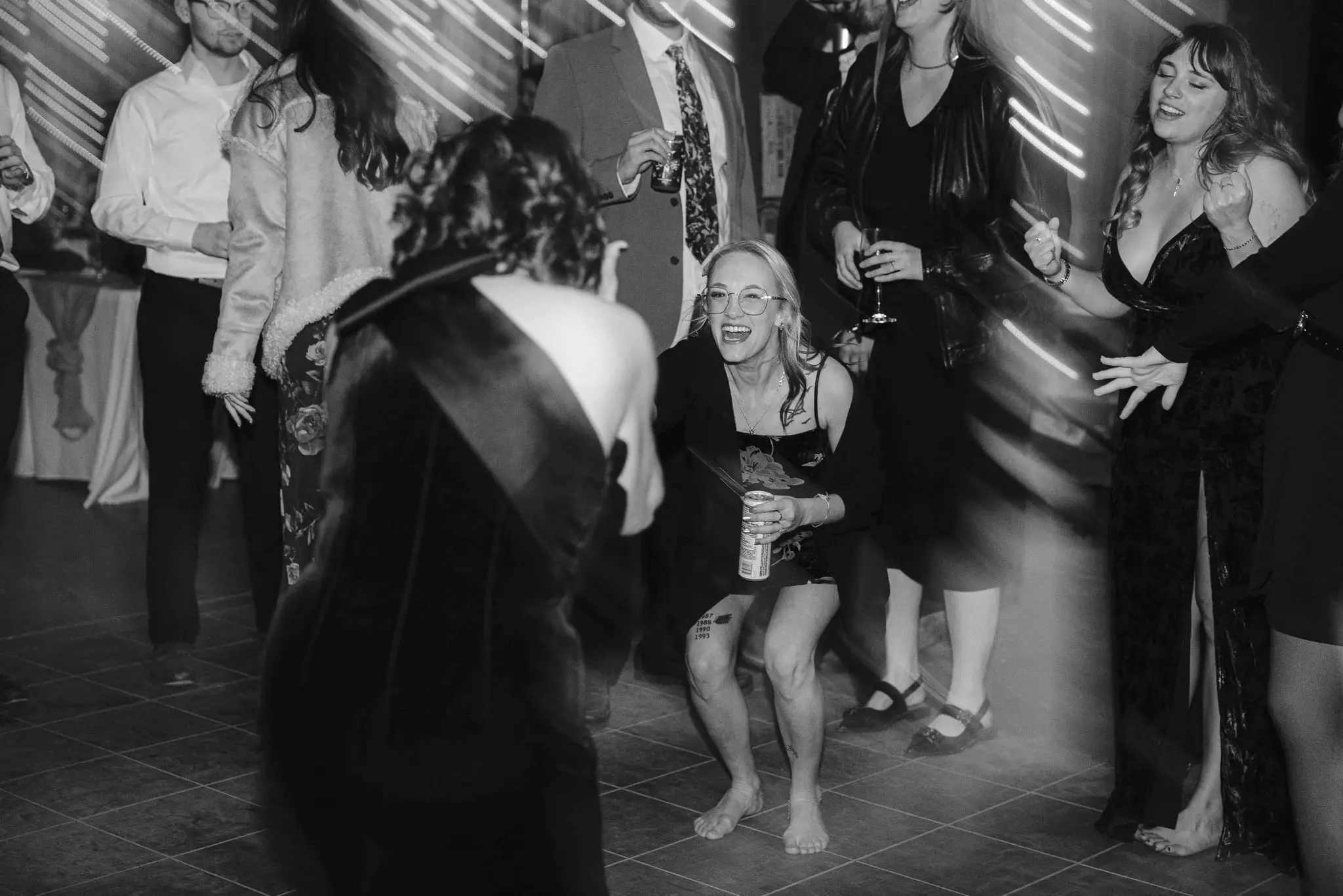 Black and white barefoot guests crouch and dance on the tiled floor at the reception