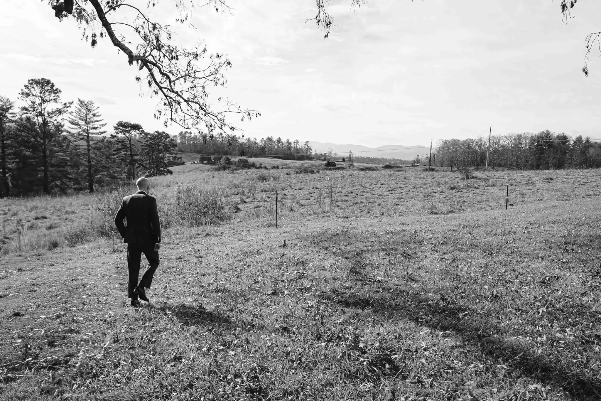 Black and white view of the groom walking alone across an open hillside field