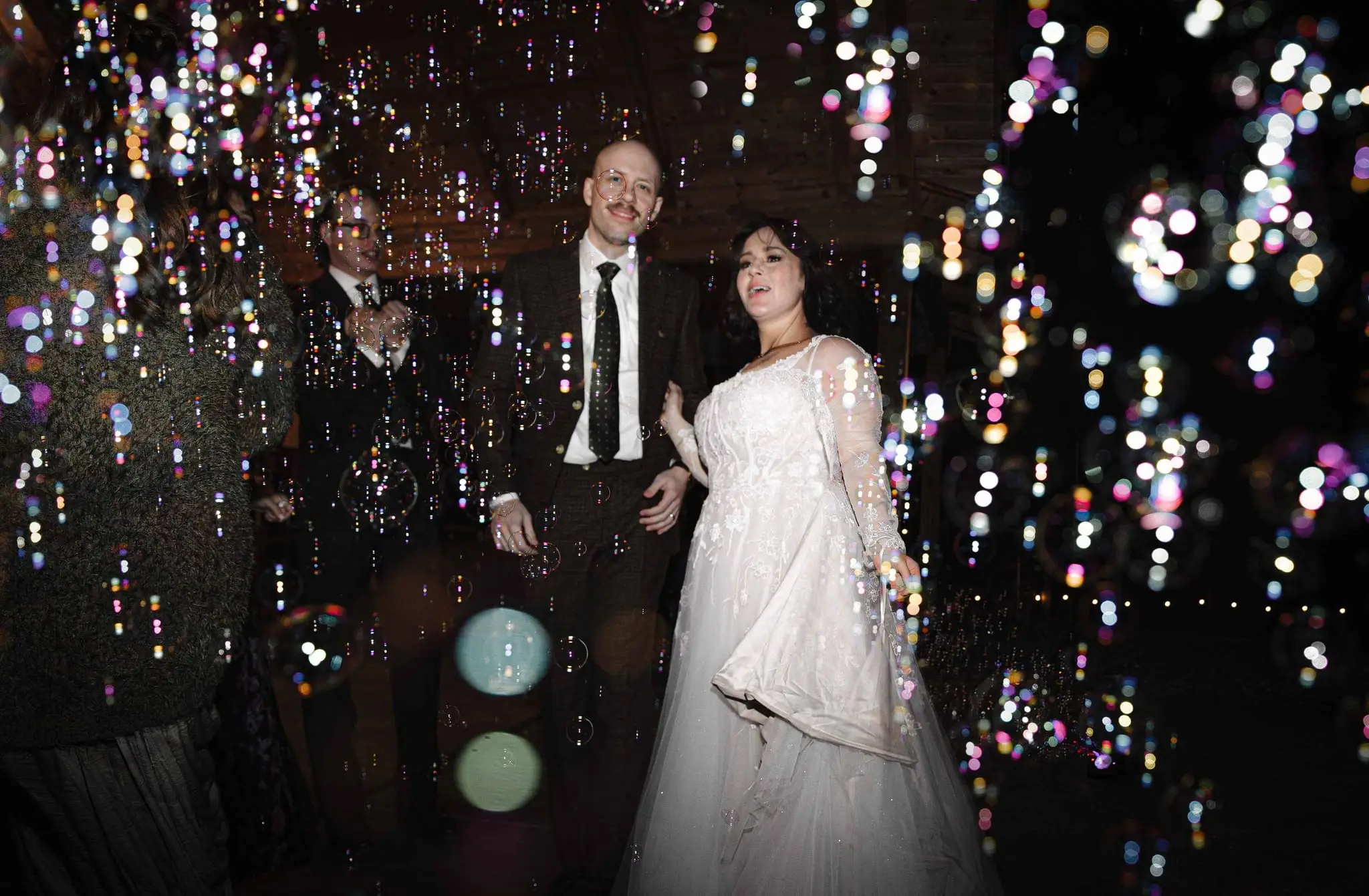 Bride in a sheer lace gown and groom in a tie surrounded by glowing bubbles at the reception