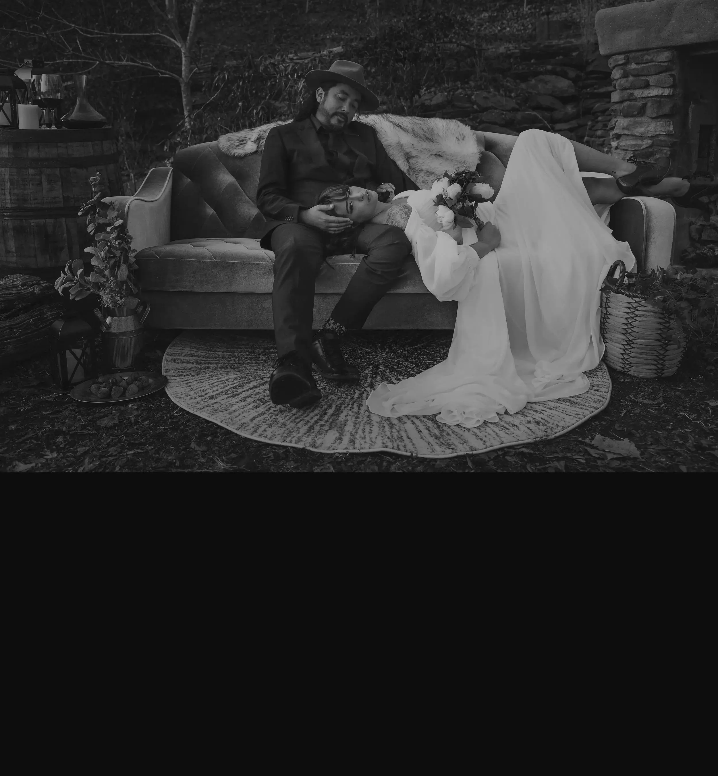A man resting his head in his partner’s lap on a vintage sofa set up outdoors on a rug