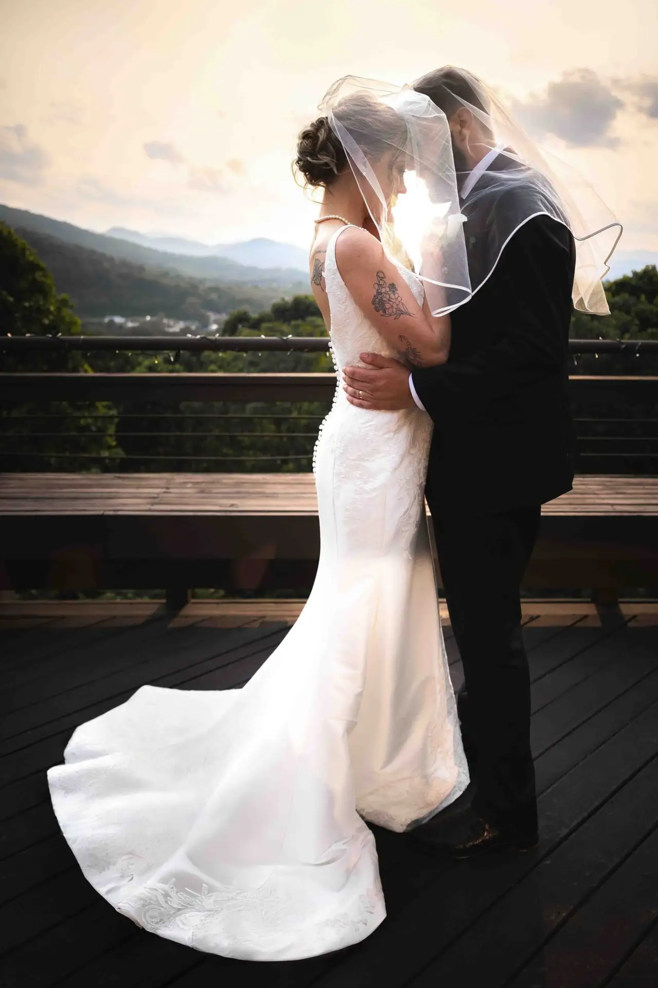 Bride and groom embracing on a deck at sunset with mountains behind them at the Crest Center