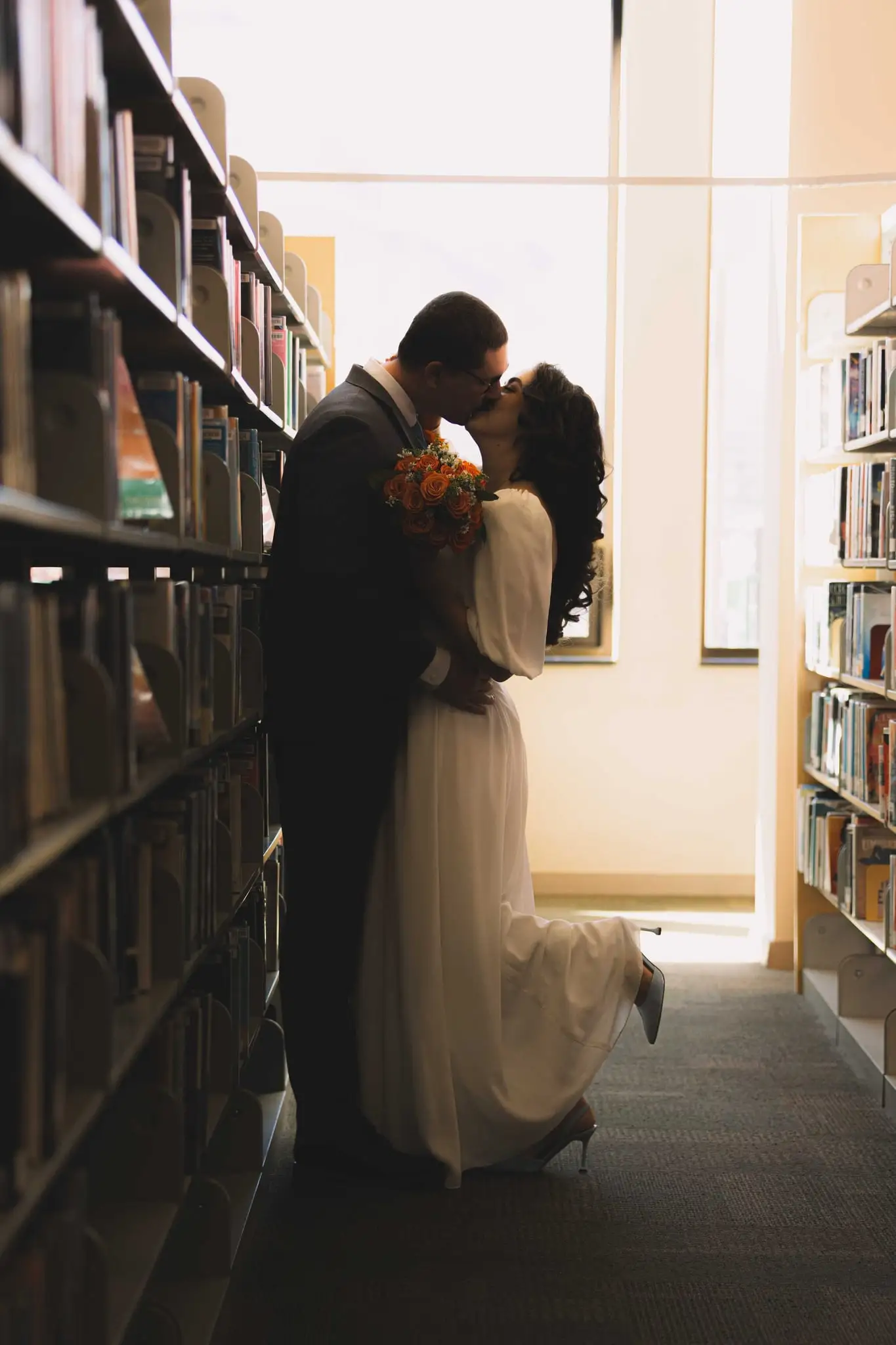 Giuliette and Will’s courthouse wedding day, Asheville NC — the couple kissing between tall library bookshelves