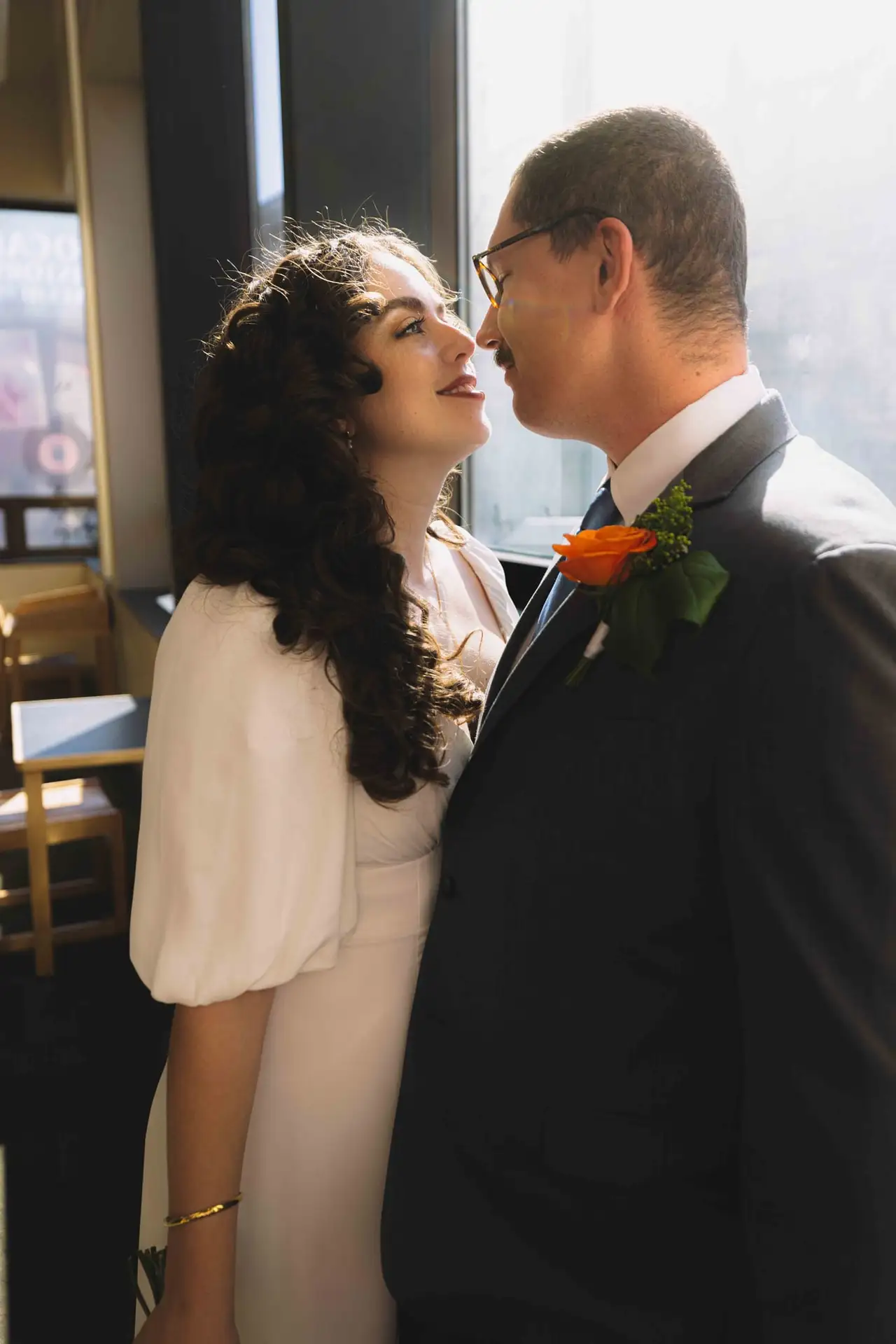 A bride laughing as her husband leans in at a window table after their courthouse ceremony in Asheville