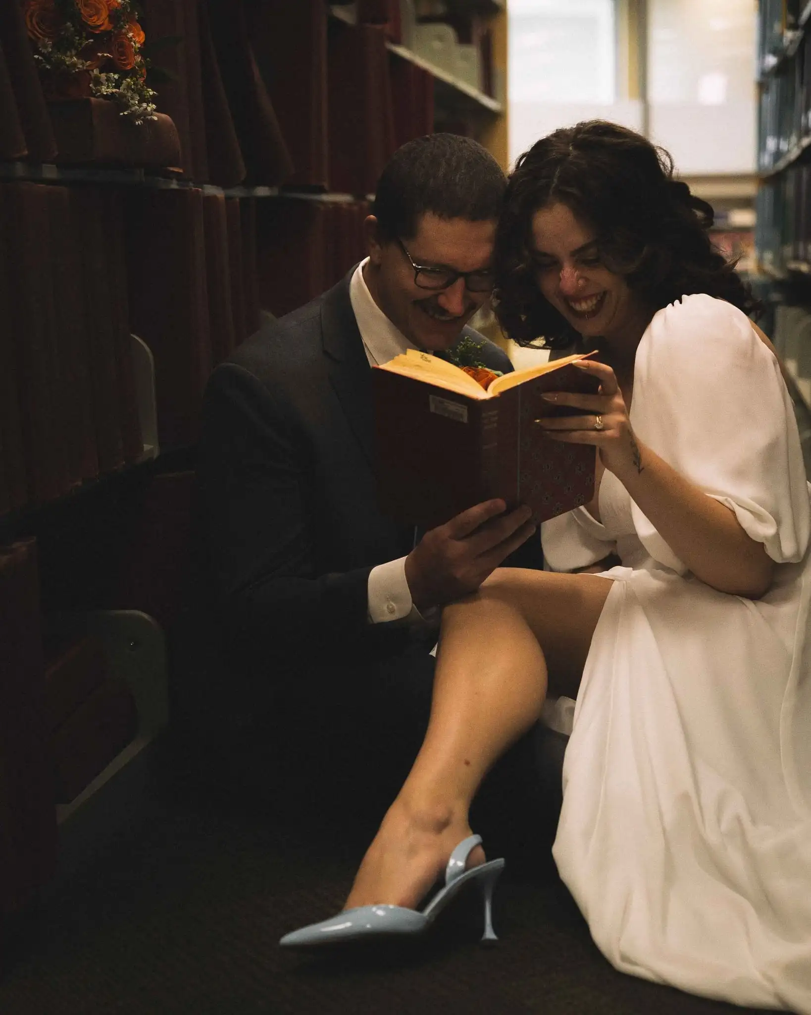 Couple laughing over an old book on the library floor after their courthouse wedding