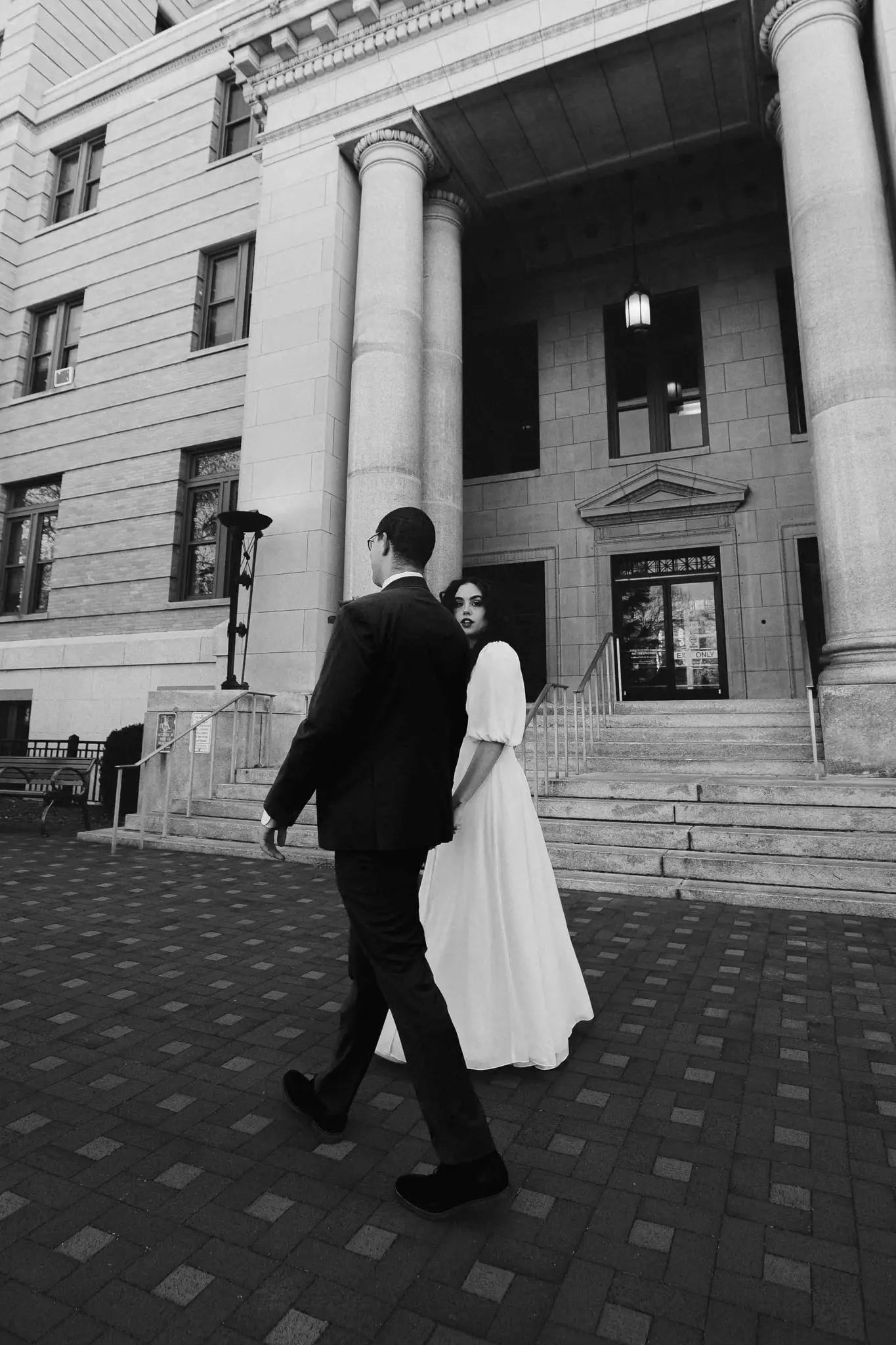 Giuliette and Will wedding at Buncombe County Courthouse, Asheville NC — the couple walking past stone columns and steps, black and white