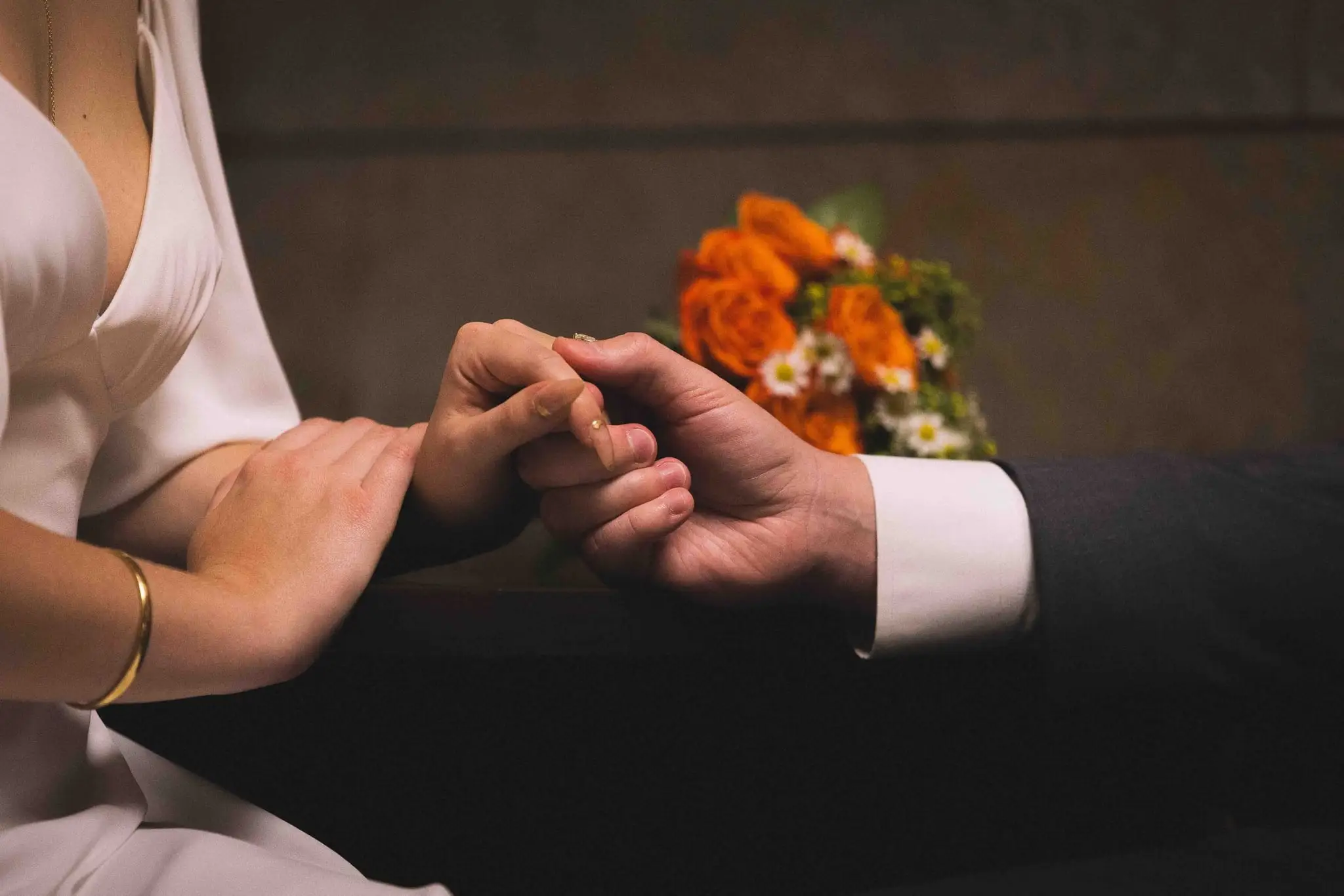 Giuliette and Will’s courthouse wedding day, Asheville NC — close view of the couple's joined hands with the bride's orange bouquet beside them