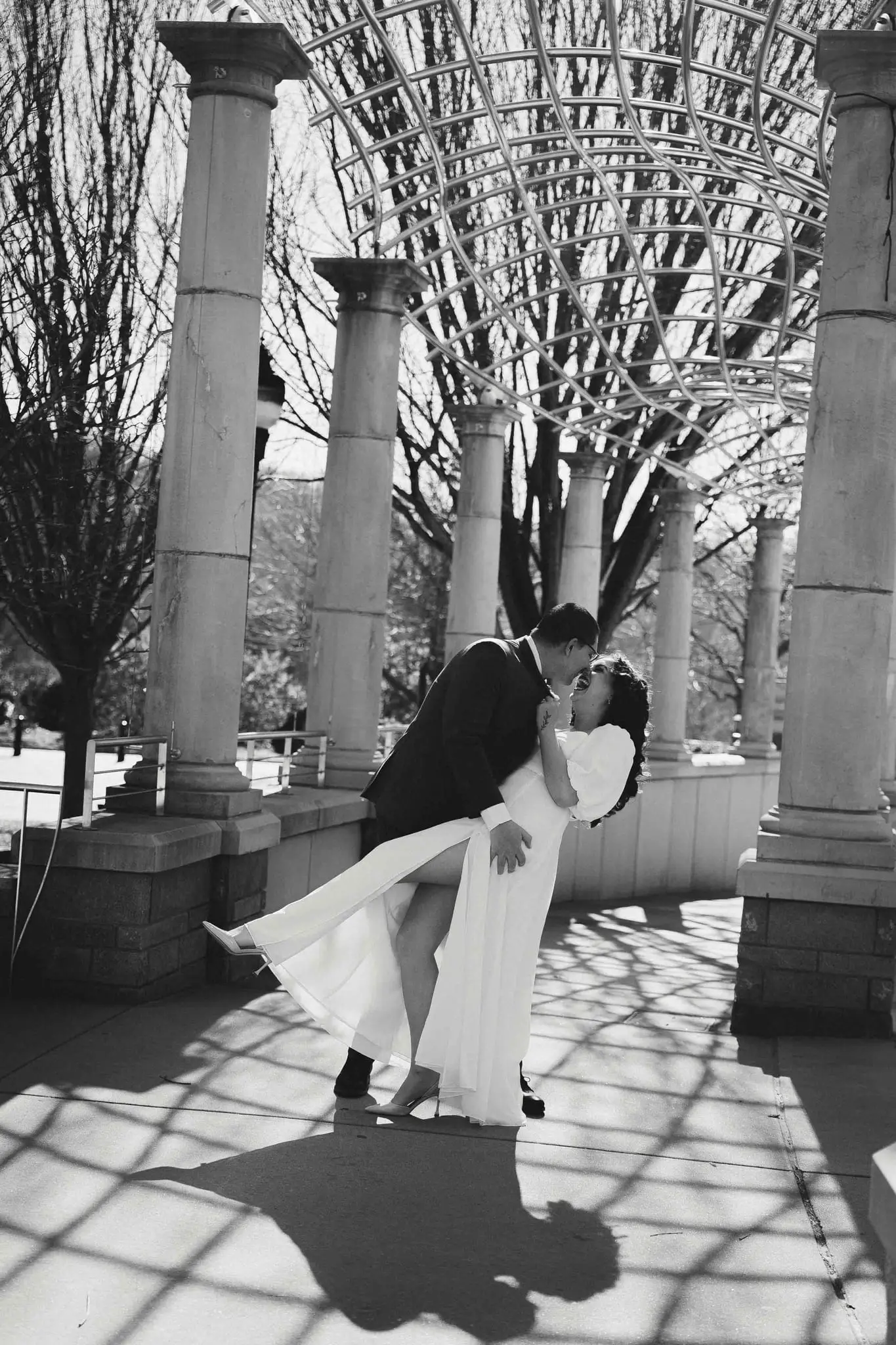 Giuliette and Will’s courthouse wedding day, Asheville NC — the groom dipping the bride in a colonnade of columns and long shadows, black and white