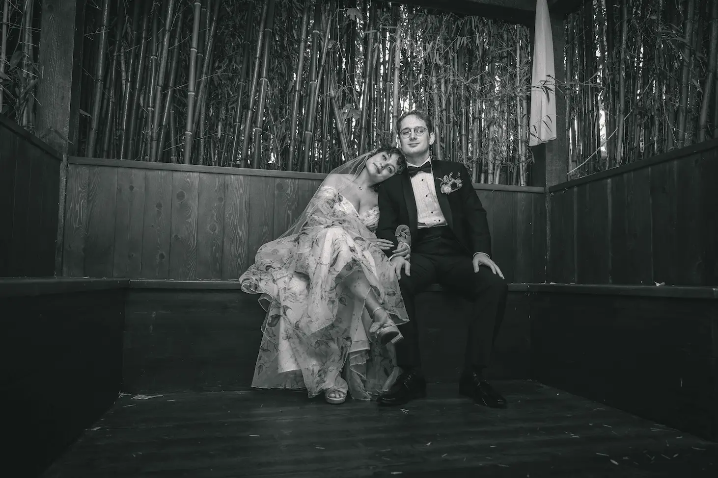 Black and white portrait of the couple seated together in a dark wooden alcove, her head on his shoulder