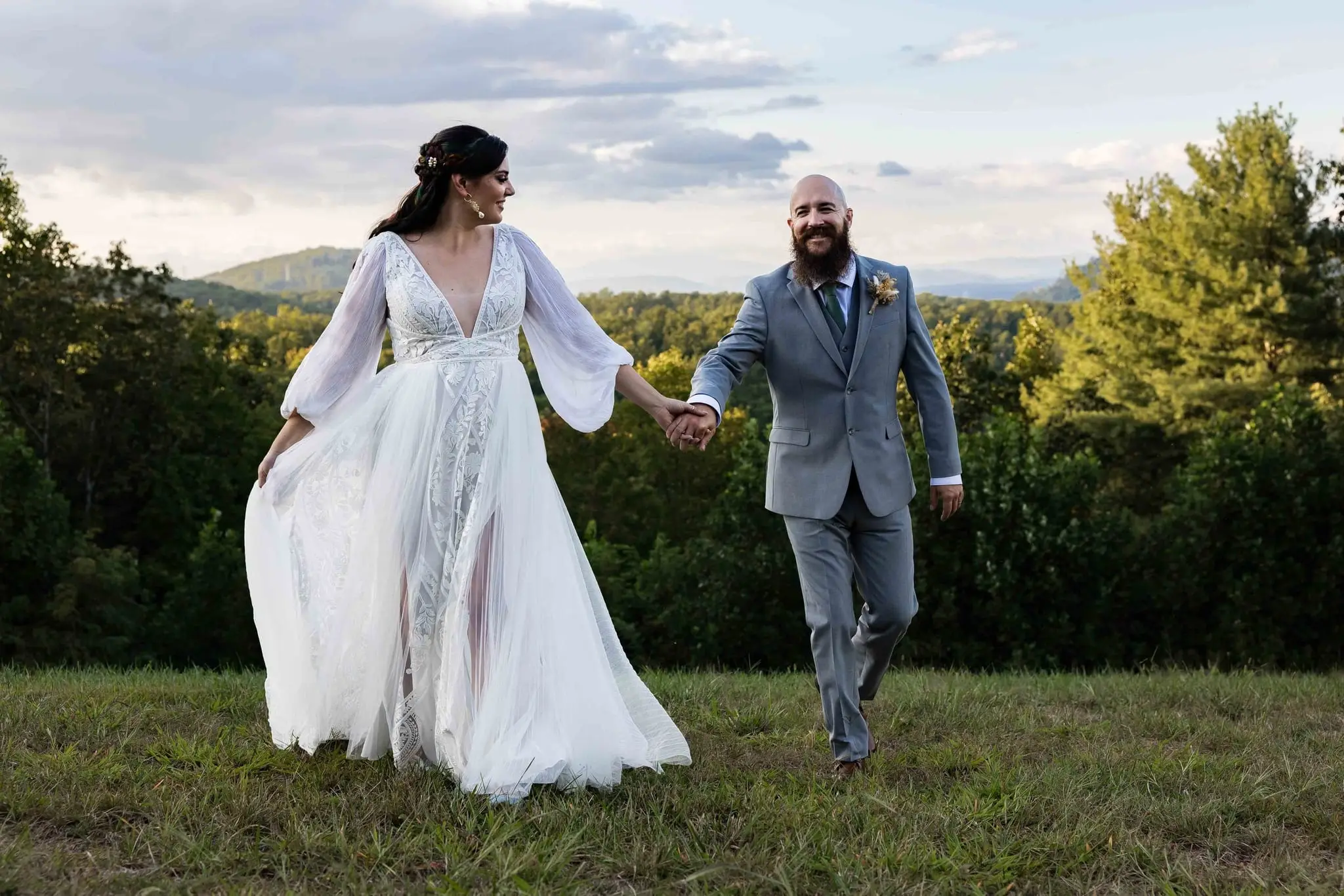 Bride smiling over her shoulder as she walks hand in hand with Brendan across the lawn