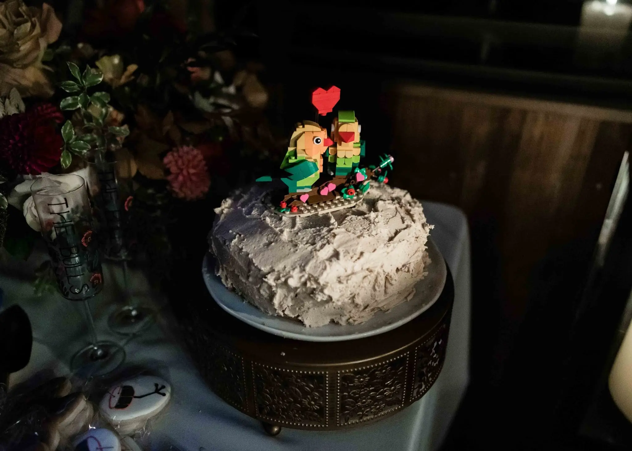 Frosted wedding cake with a playful pixel-style lovebird topper and a red heart