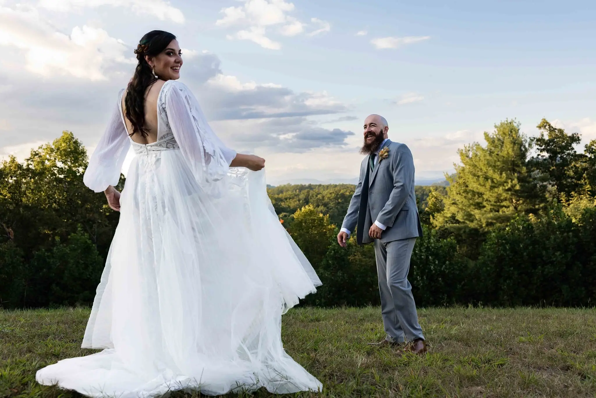 Bride lifting her skirt and laughing as the groom steps back on the hilltop