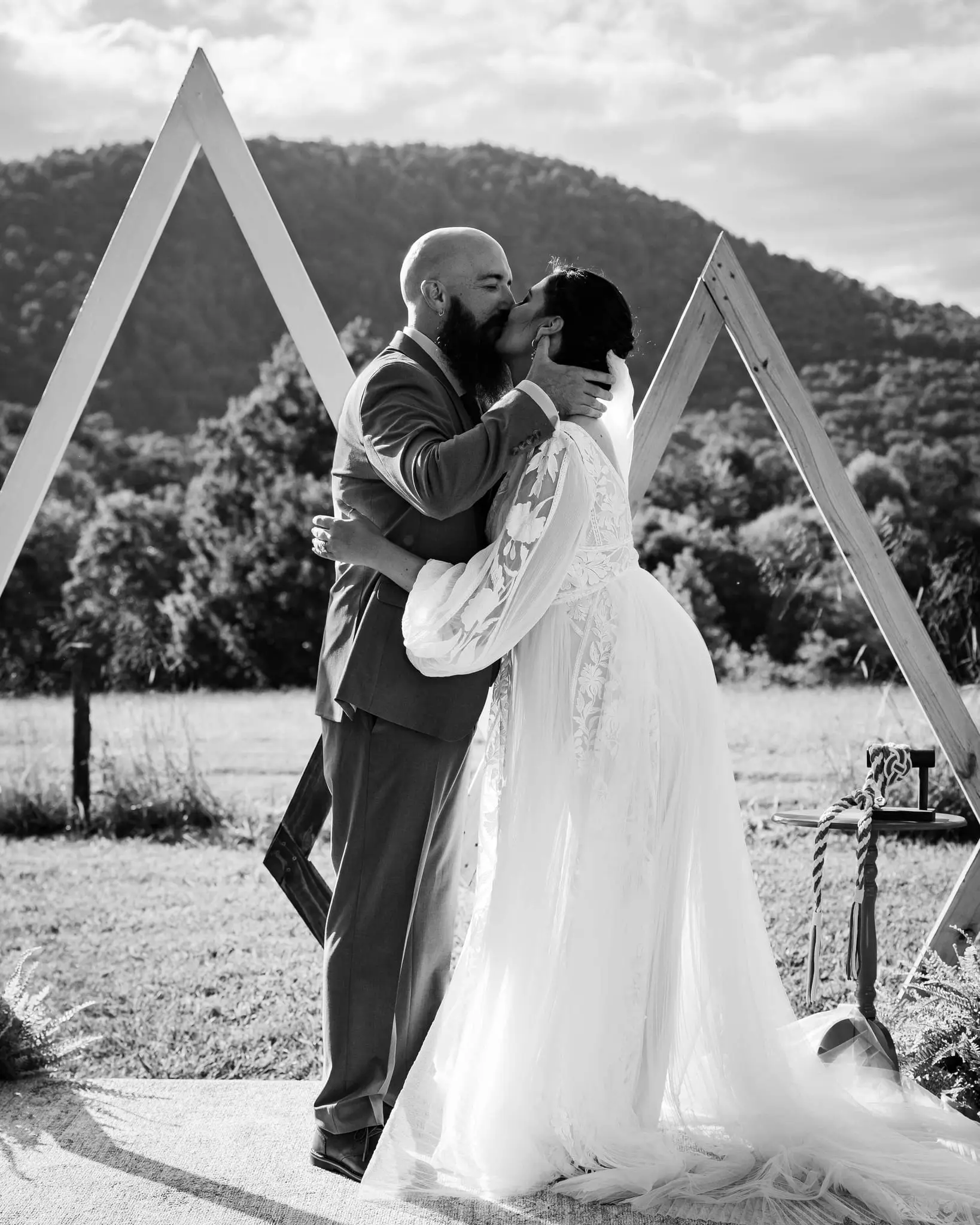 Black and white kiss as newlyweds in front of the arch with a mountain ridge behind
