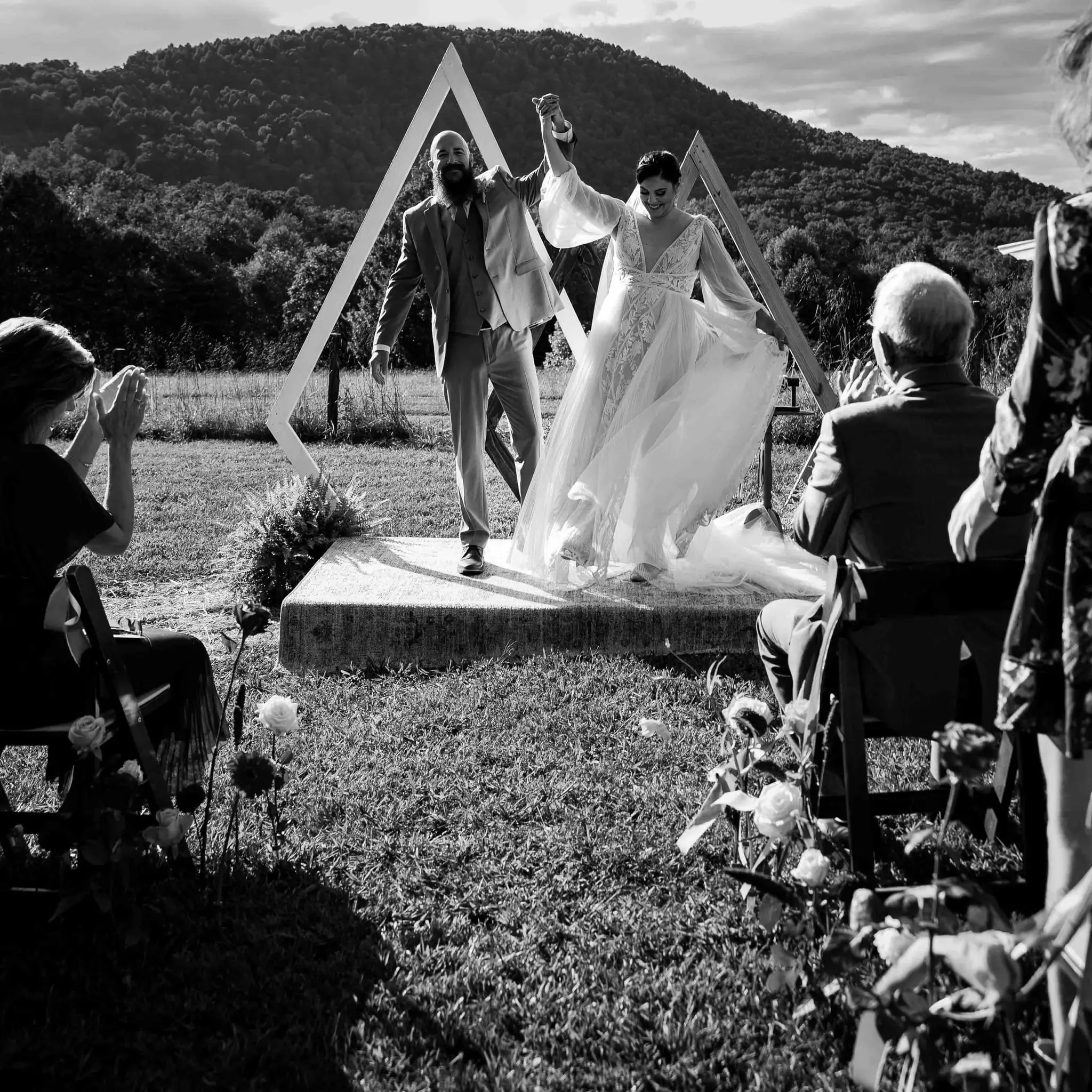 Black and white of the couple raising joined hands and stepping off the platform as guests cheer