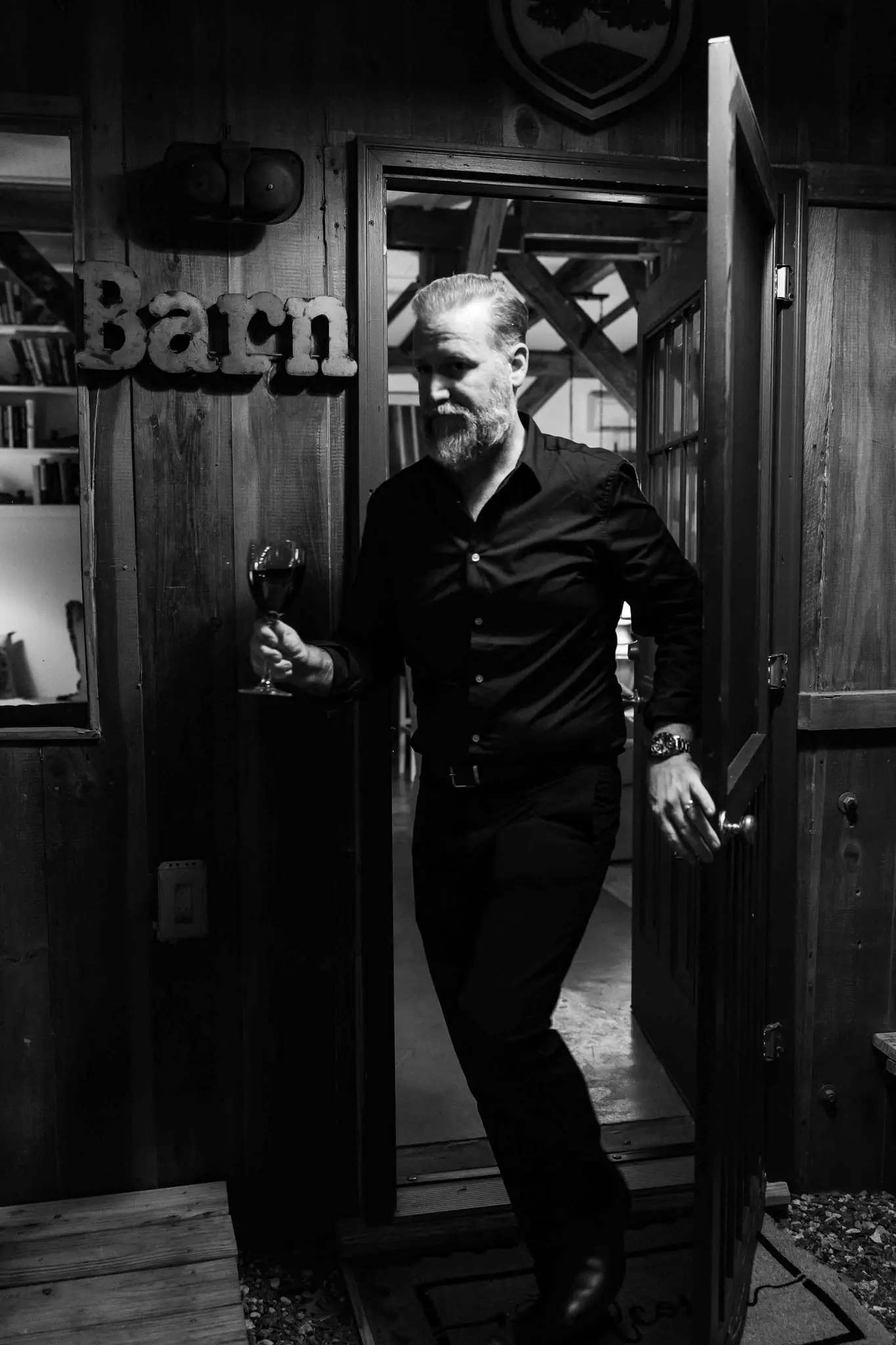 Black and white of a guest holding a glass of wine as he steps through the barn door