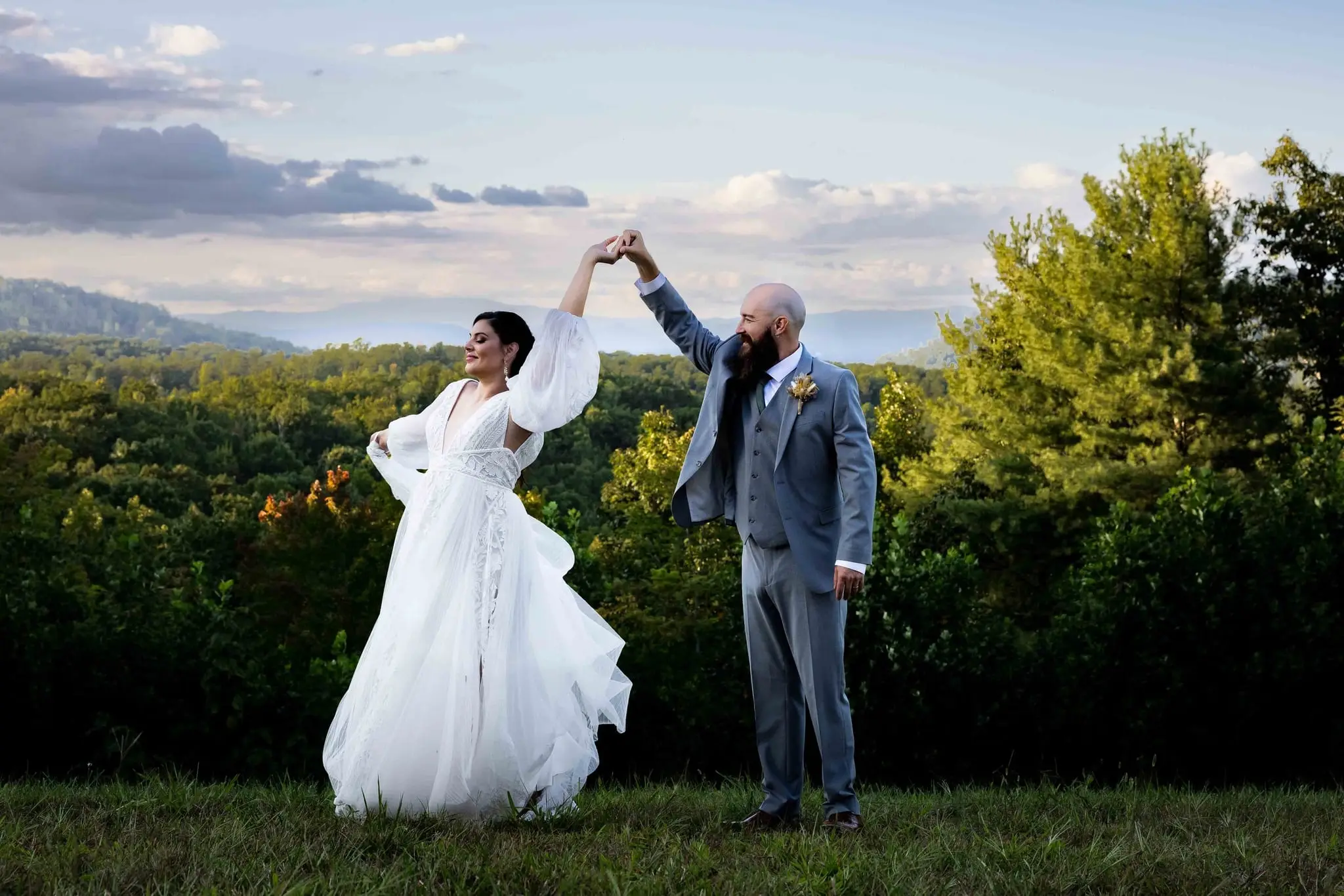 Groom twirling the bride on a grassy overlook with layered Blue Ridge ridgelines behind