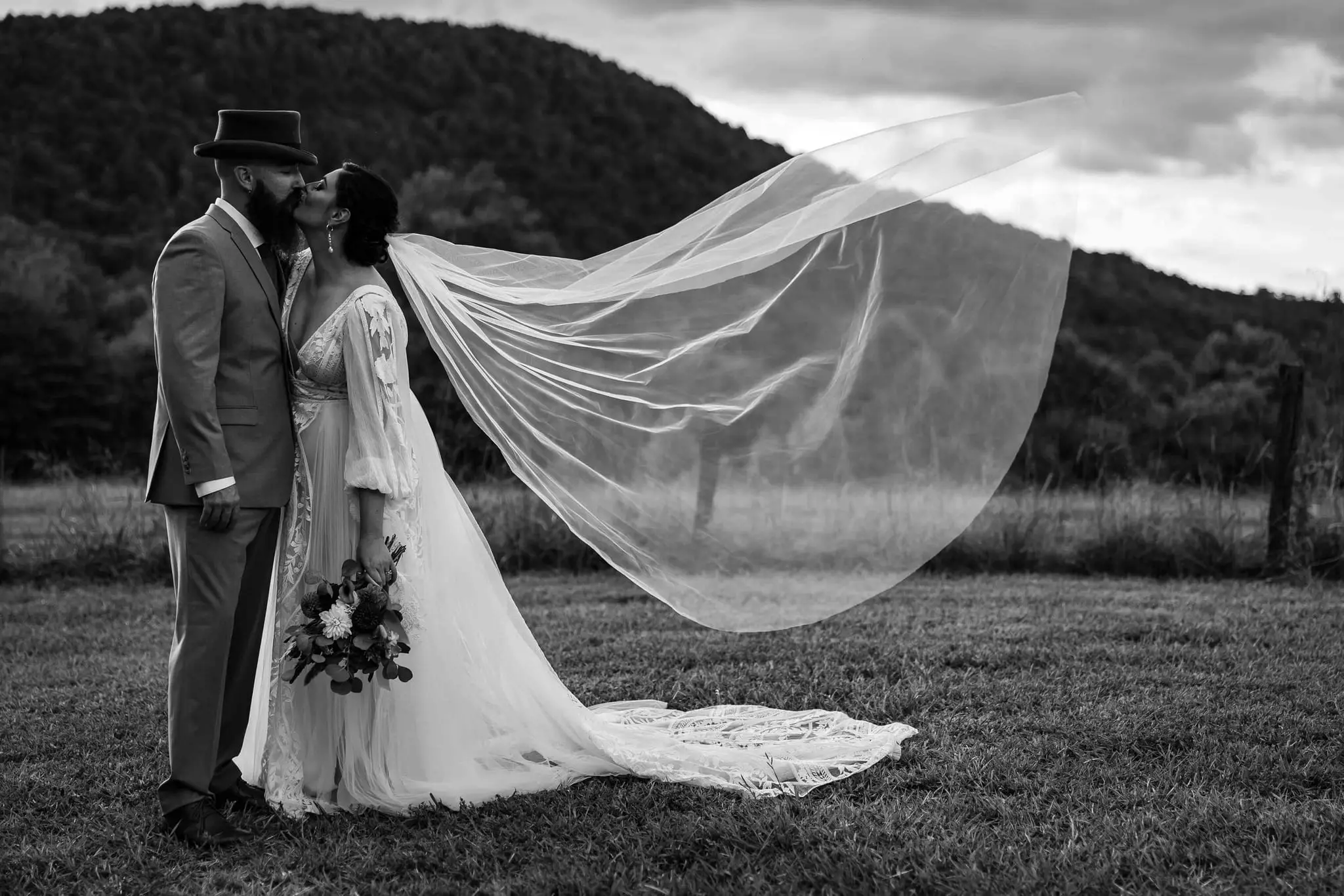 Black and white kiss in a mountain meadow as the wind lifts the bride's long veil