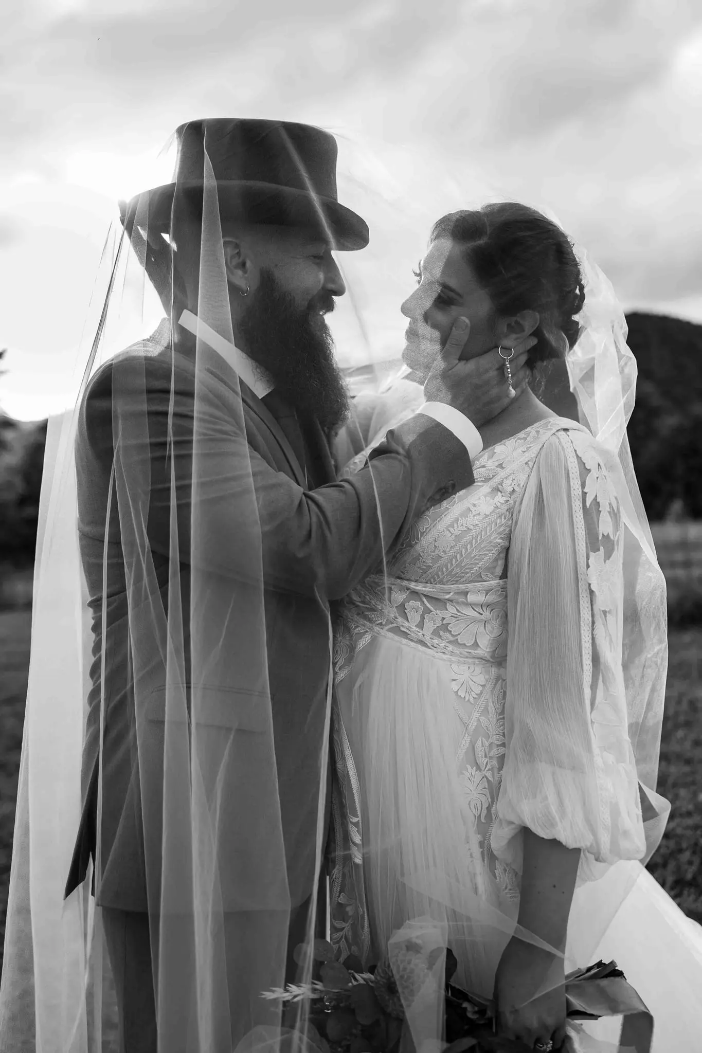Black and white of the groom in a top hat touching the bride's cheek beneath a sheer veil