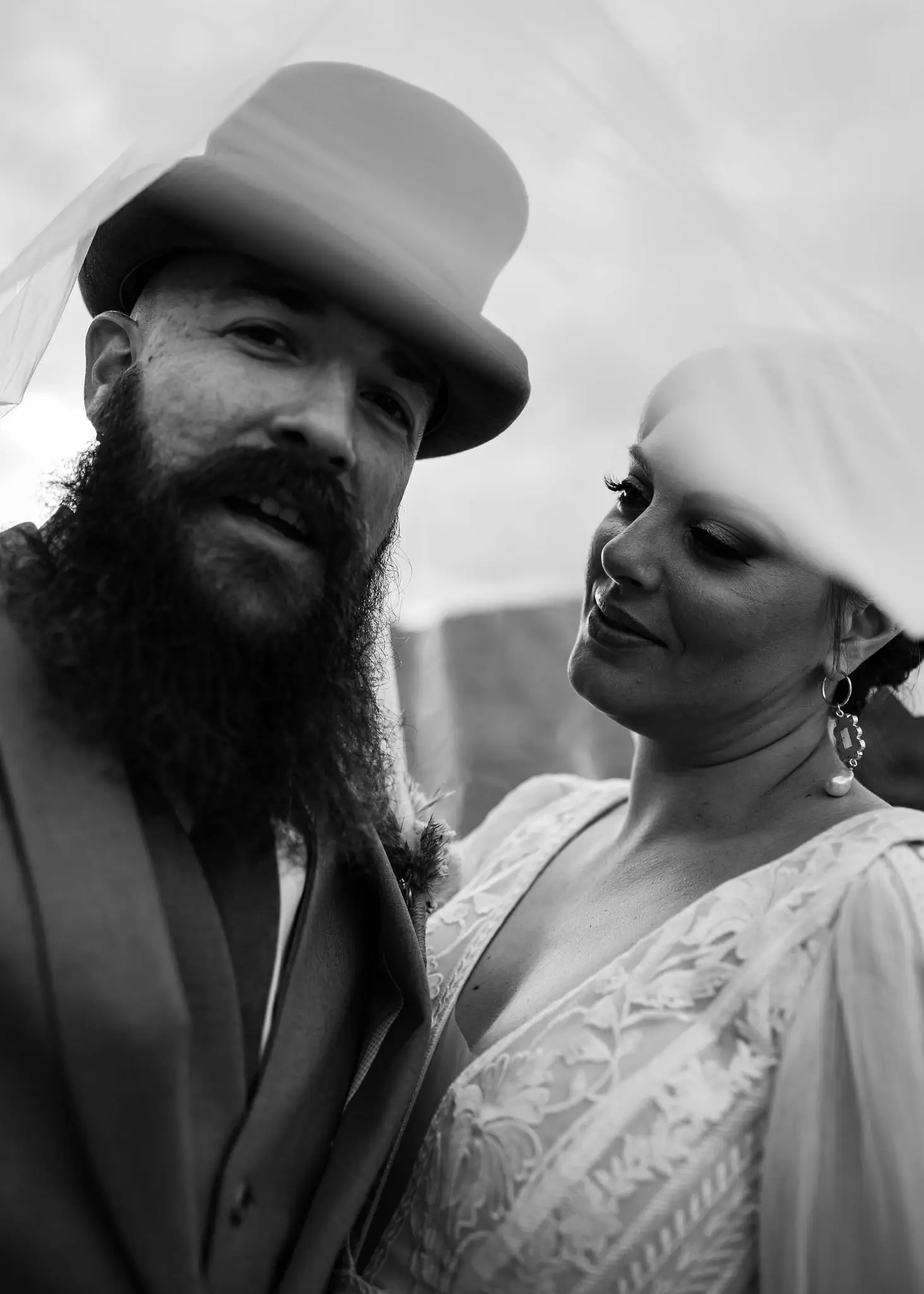Black and white close-up of the groom in a top hat as the bride looks on beneath her veil