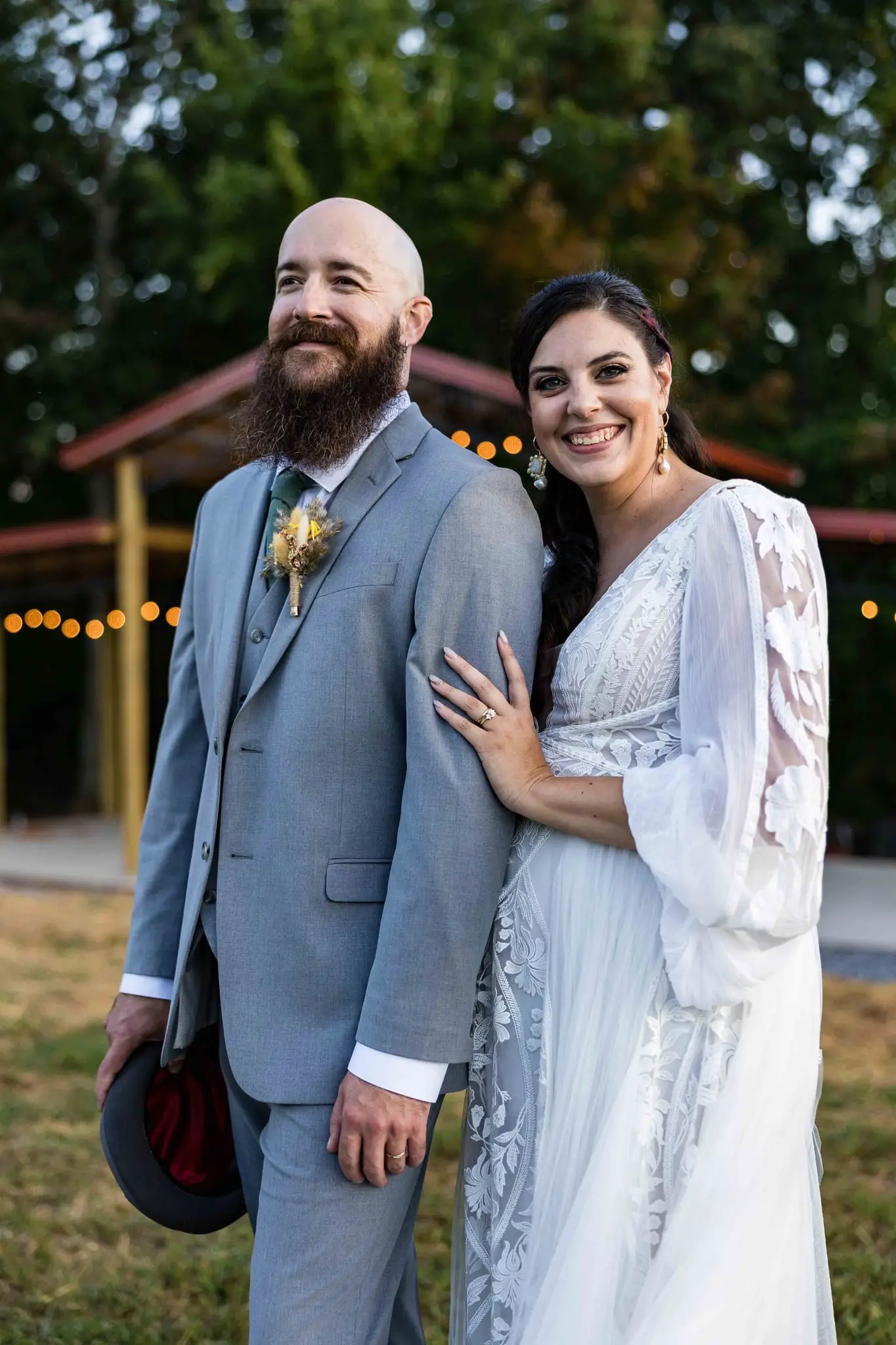 Megan and Brendan standing close with her ring hand on his sleeve, a lit pavilion behind them