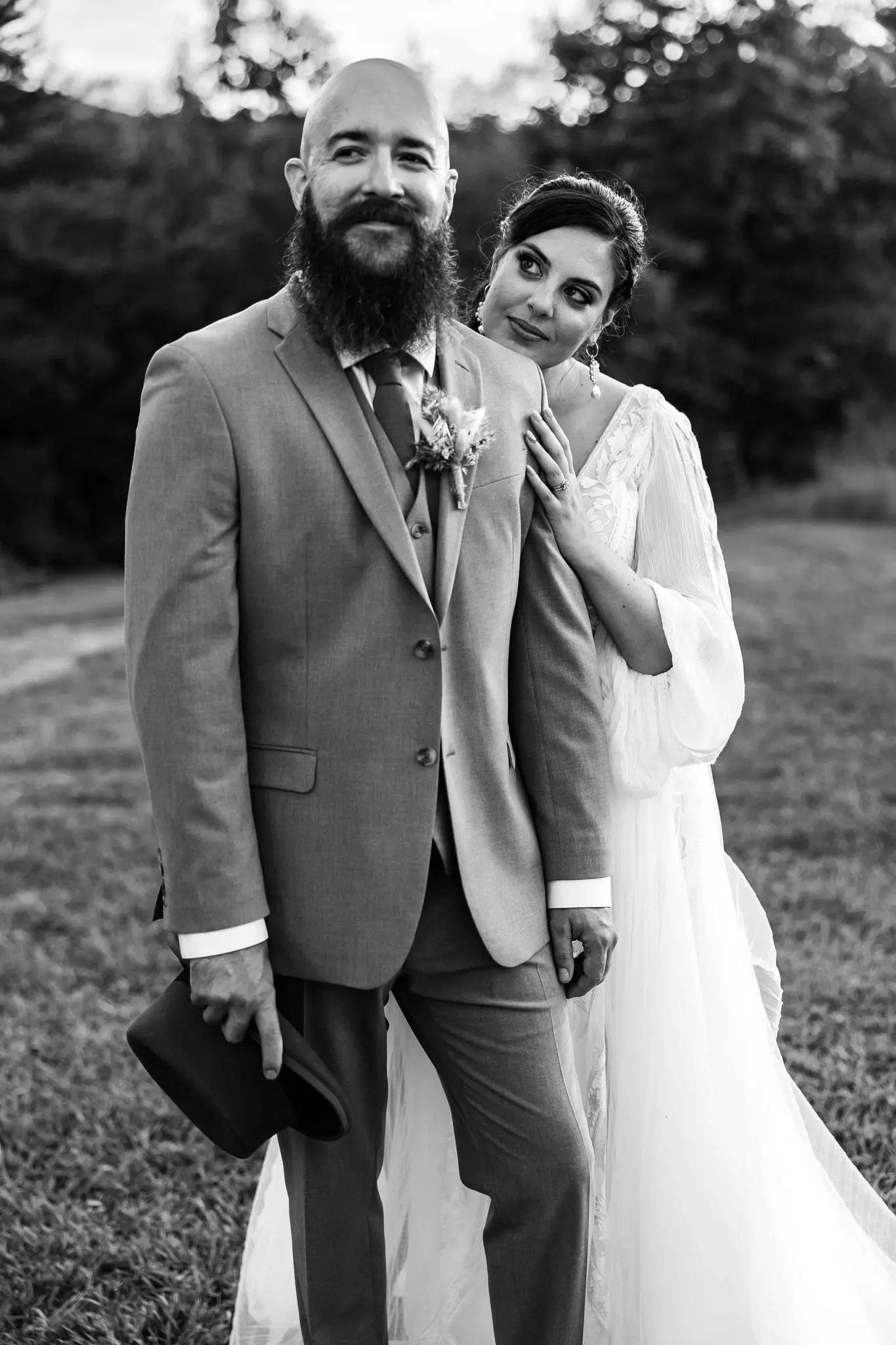Black and white of the bride resting her cheek on the groom's shoulder, his hat in his hand