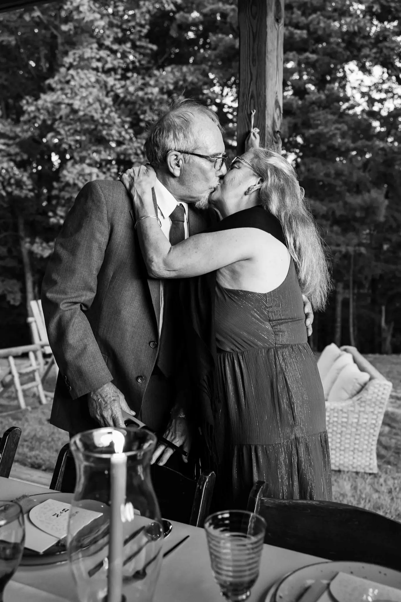 Black and white of two wedding guests sharing a kiss beside a candlelit table