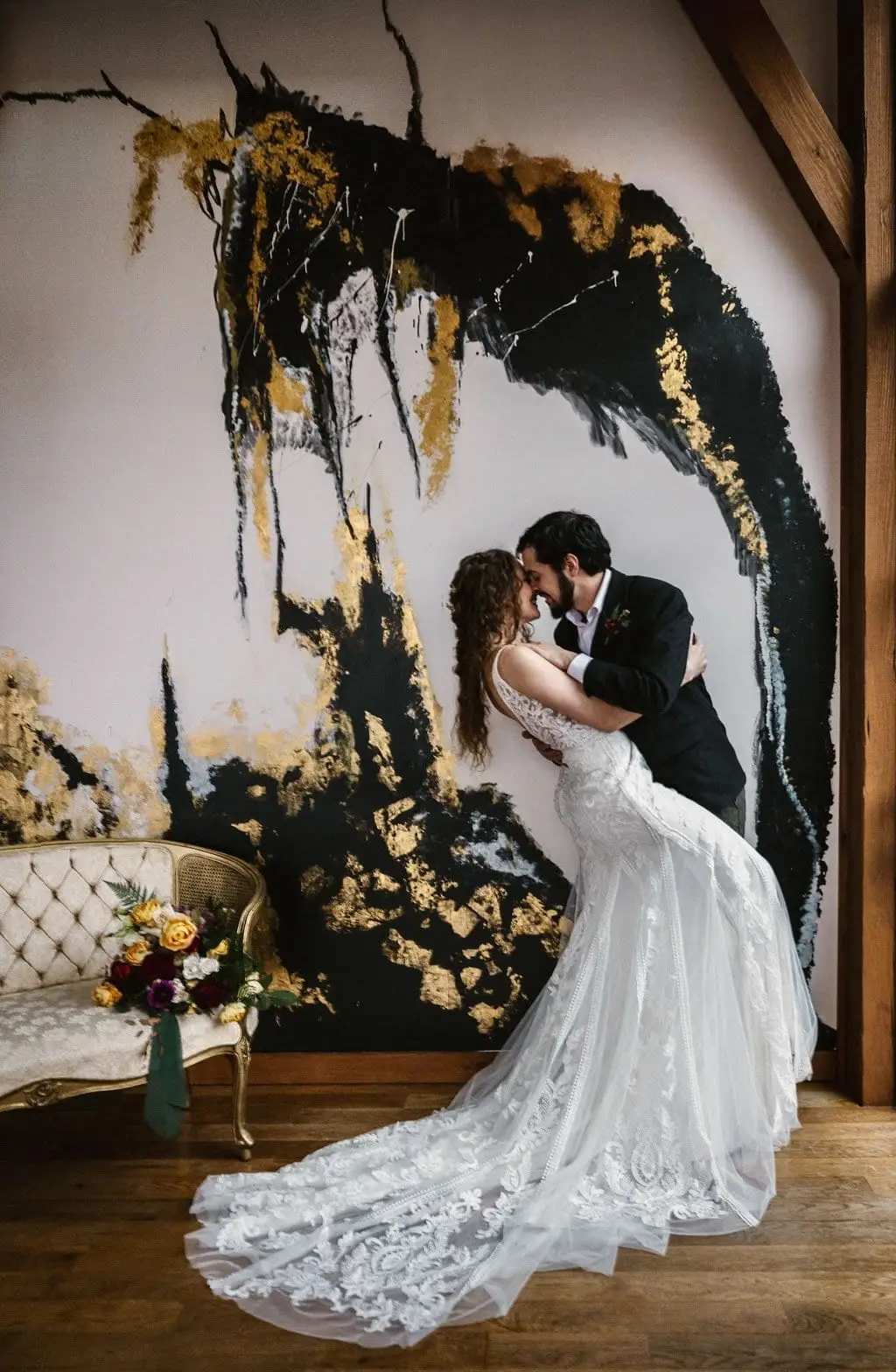 Joe and Julia sharing a dipped kiss in front of an abstract gold and black wall at Haiku I Do