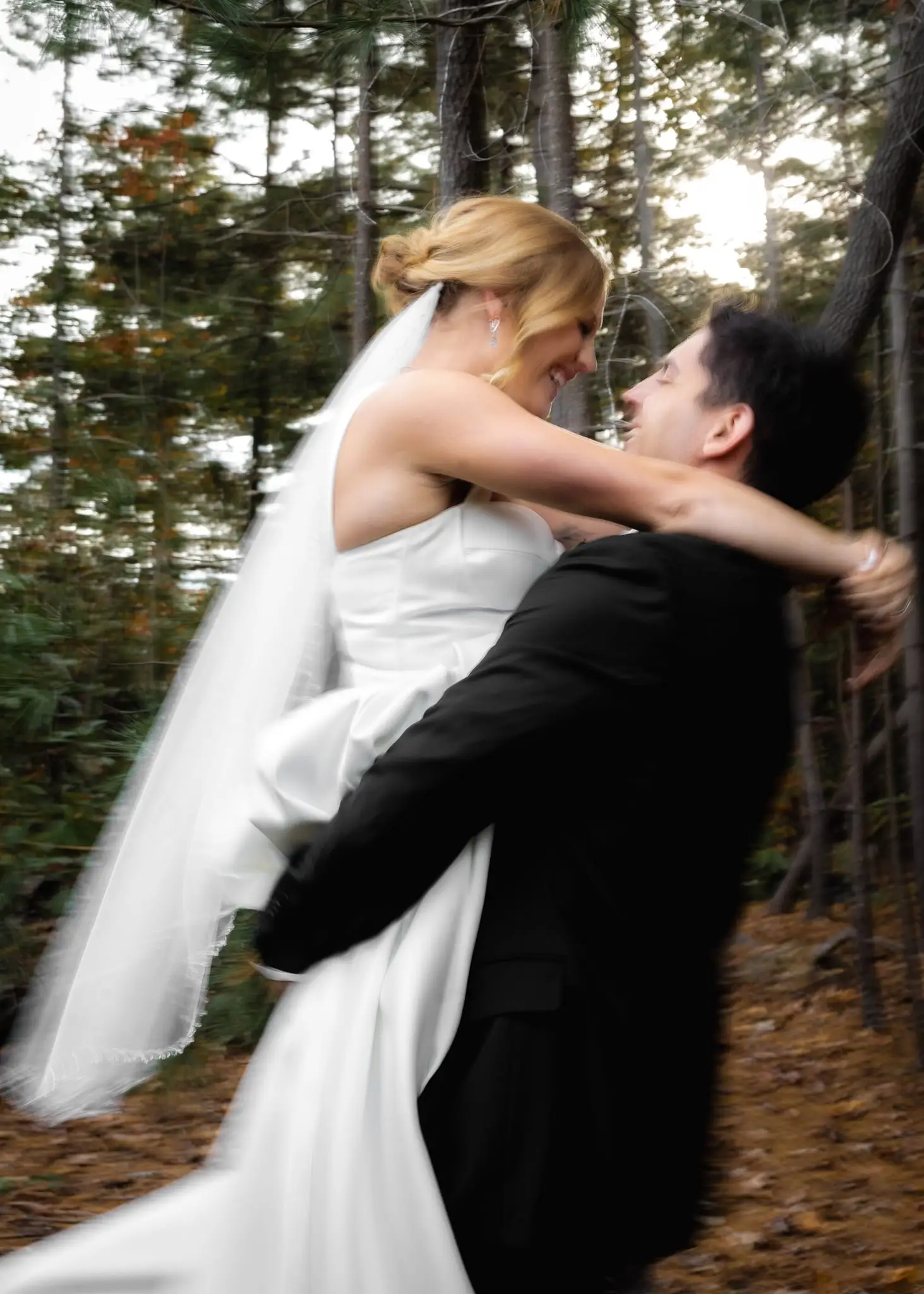 Groom lifting the bride in an autumn forest, her veil trailing, in warm motion blur