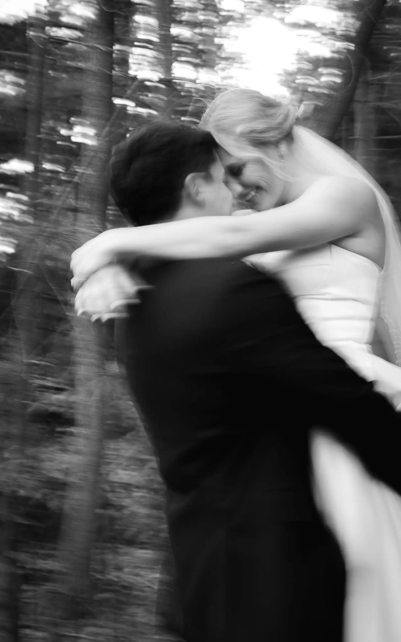 Black and white motion-blur portrait of Damian lifting Lauren in the woods near The Lodge in Flat Rock