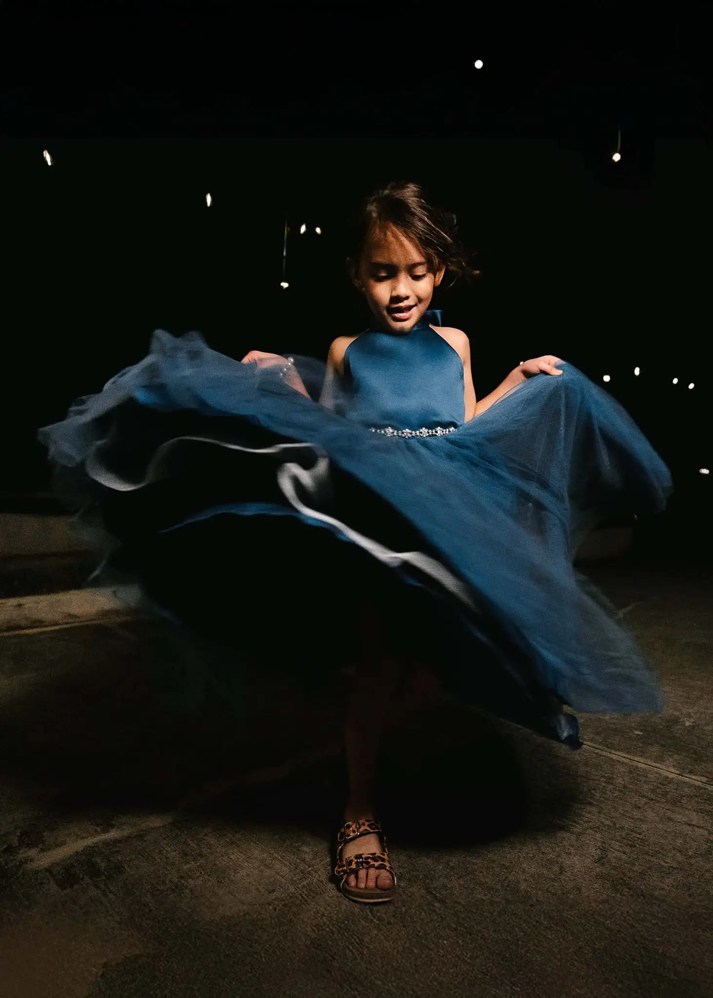Young girl in a blue tulle dress twirling in the dark with her skirt fanned out