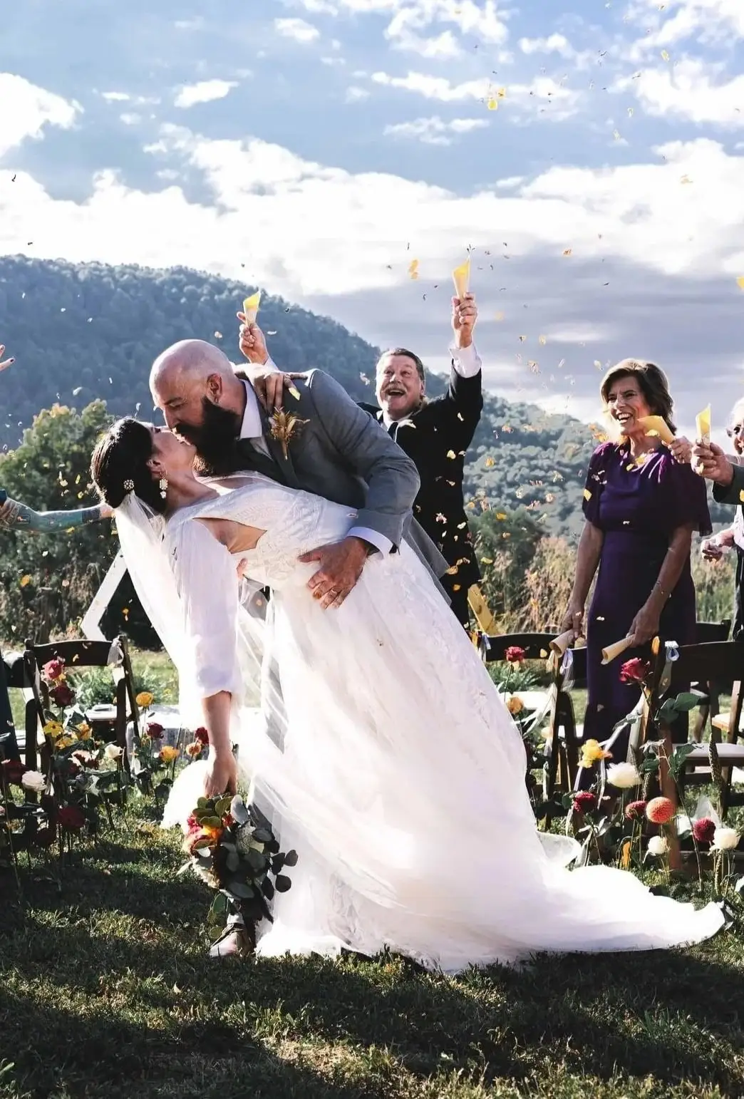 Bride and groom kiss in a dip as guests throw confetti at an outdoor mountain ceremony