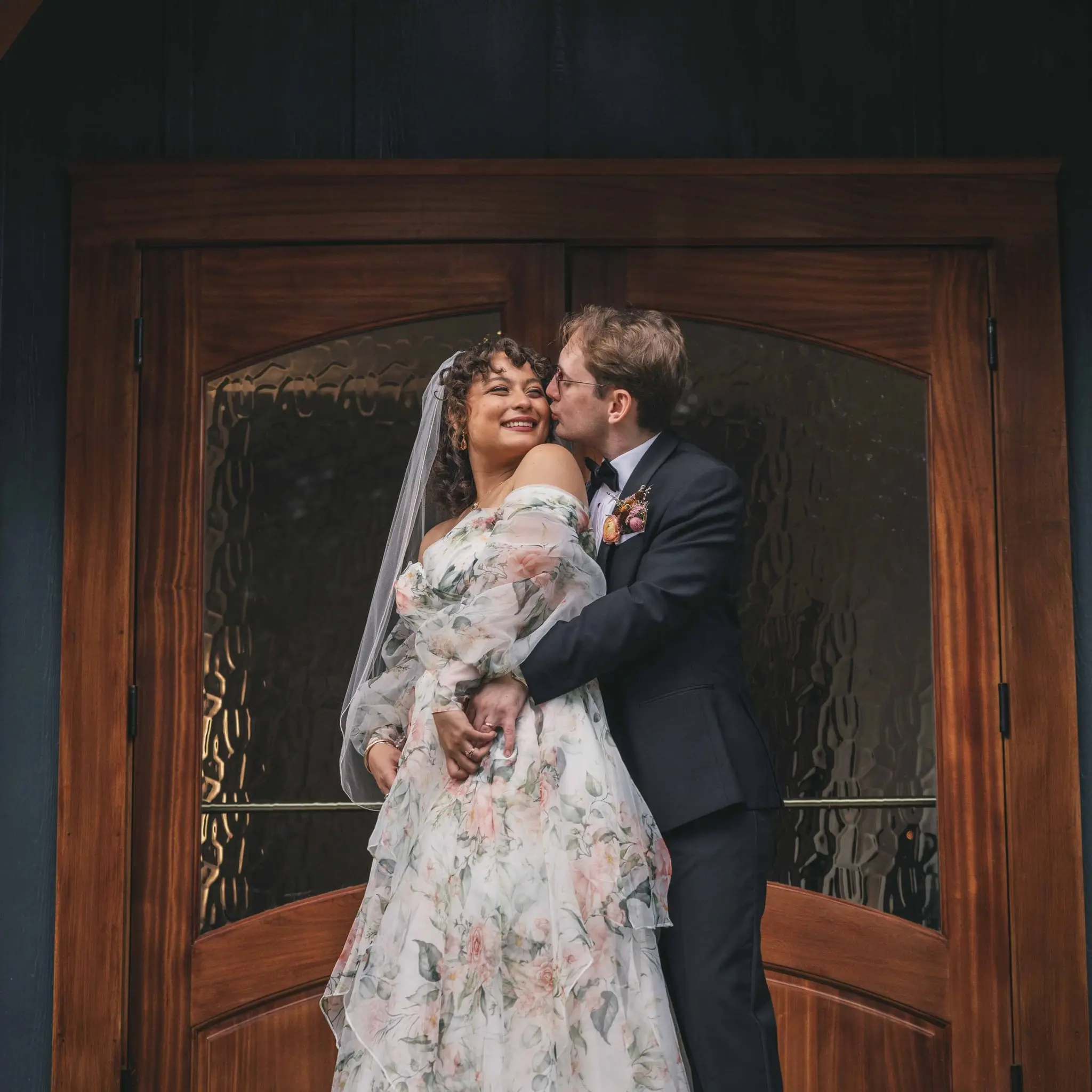 Bride and groom embracing in front of a carved wooden door at Weaver House